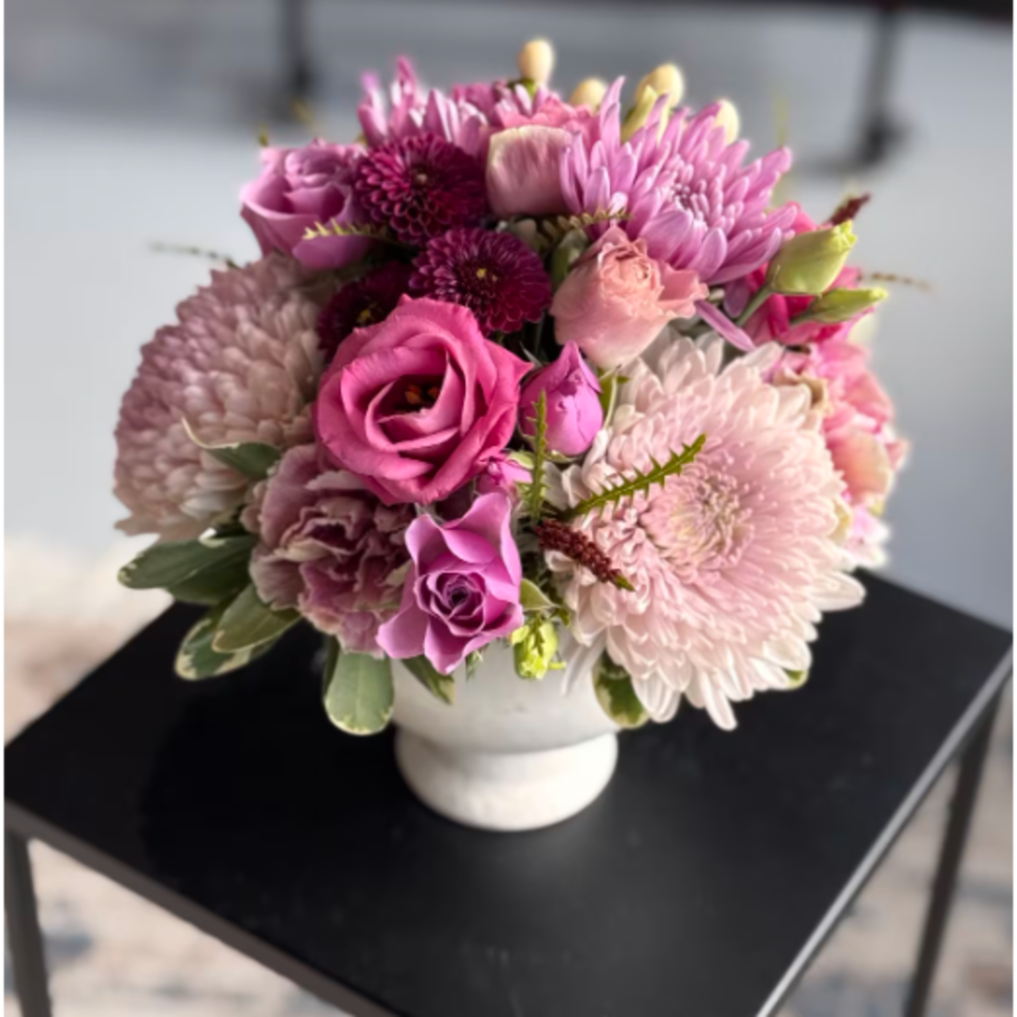 Compact arrangement of pink and purple roses and mums in a white ceramic vase