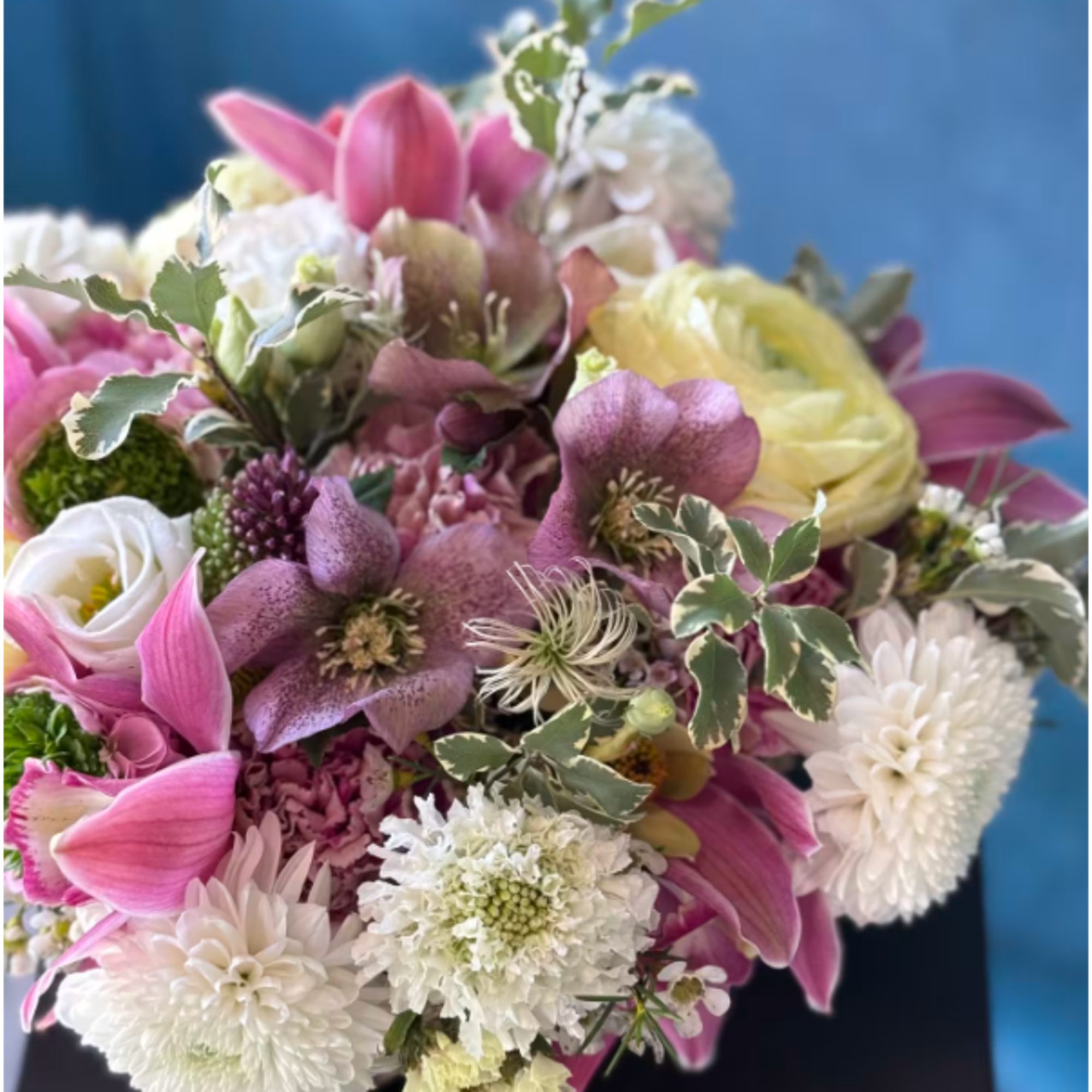 Compact arrangement of pink and white flowers with touches of yellow against a blue background