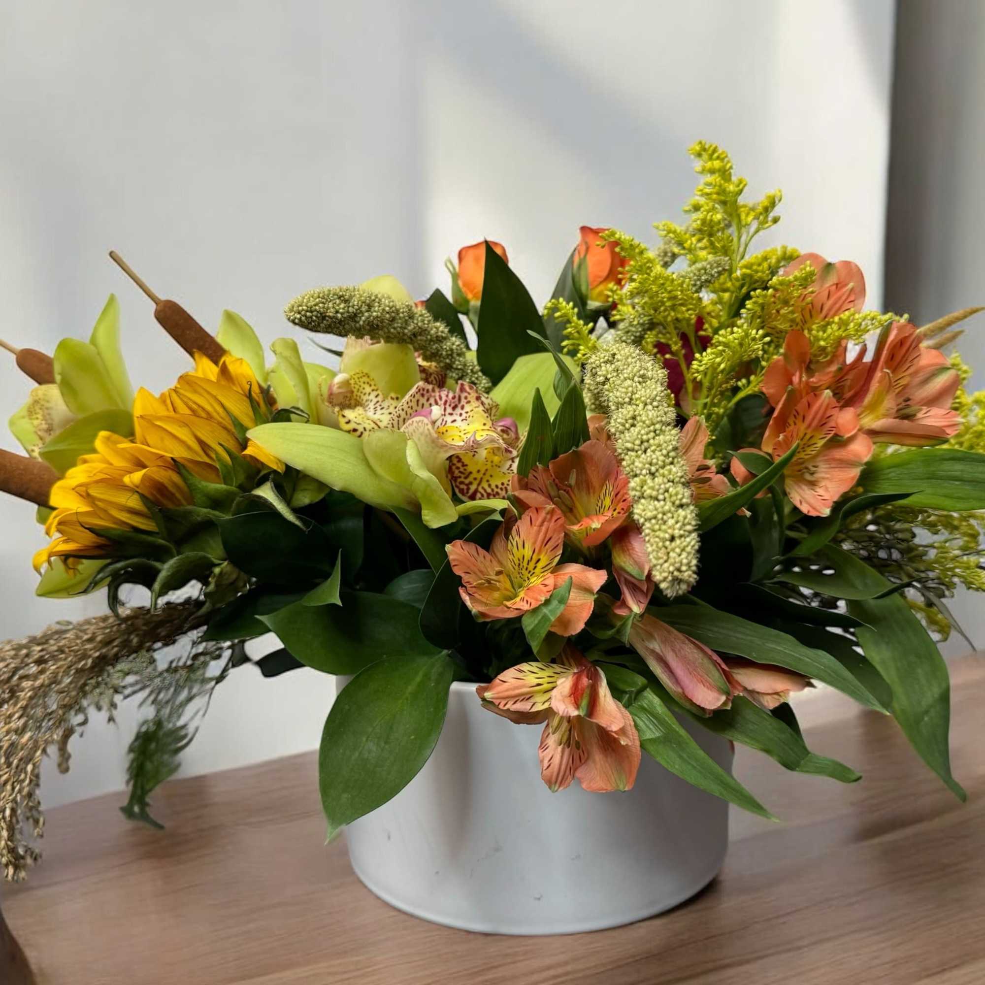Mixed floral arrangement in a white container with yellow and peach blooms