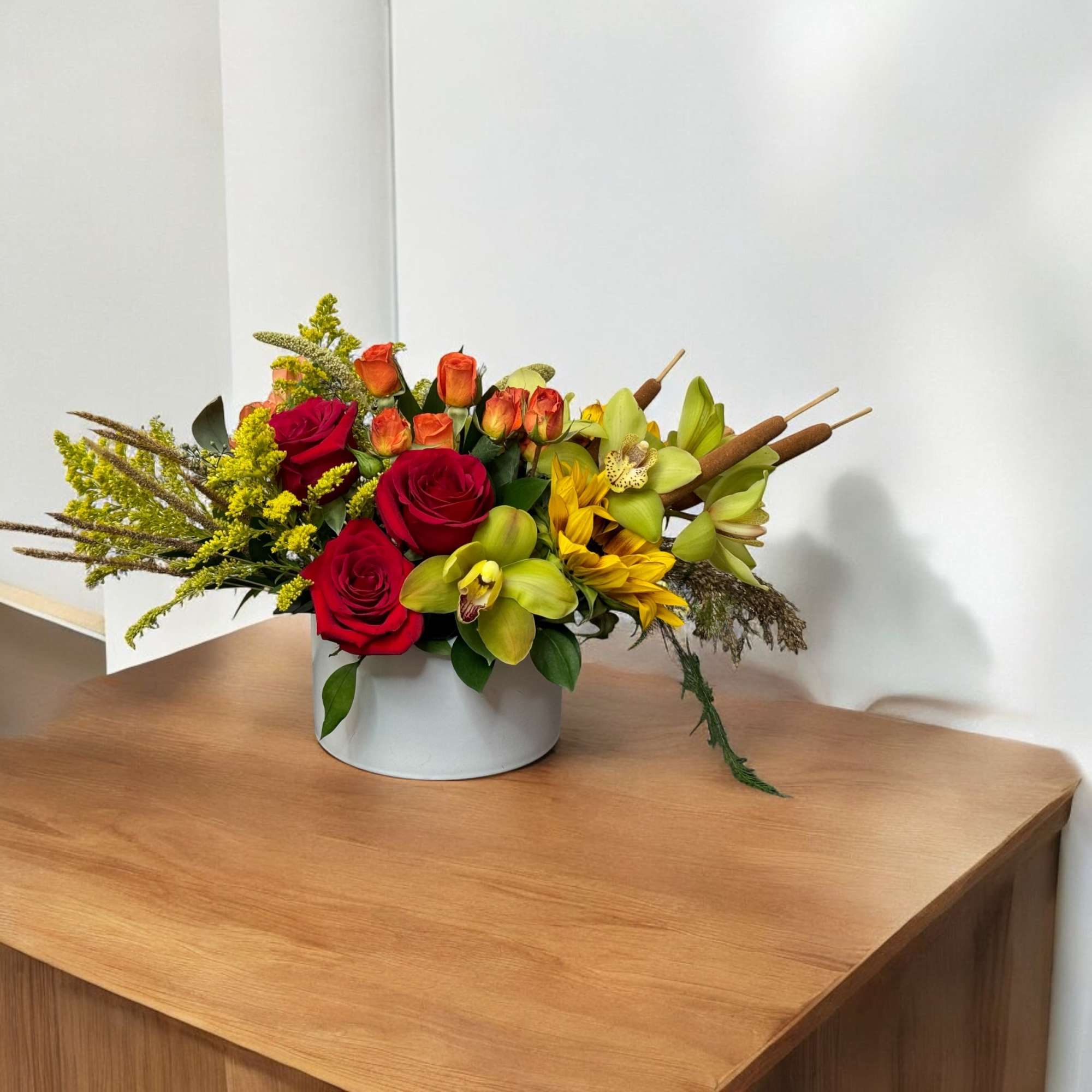 Mixed floral arrangement with red roses, yellow orchids, and sunflowers in a white container