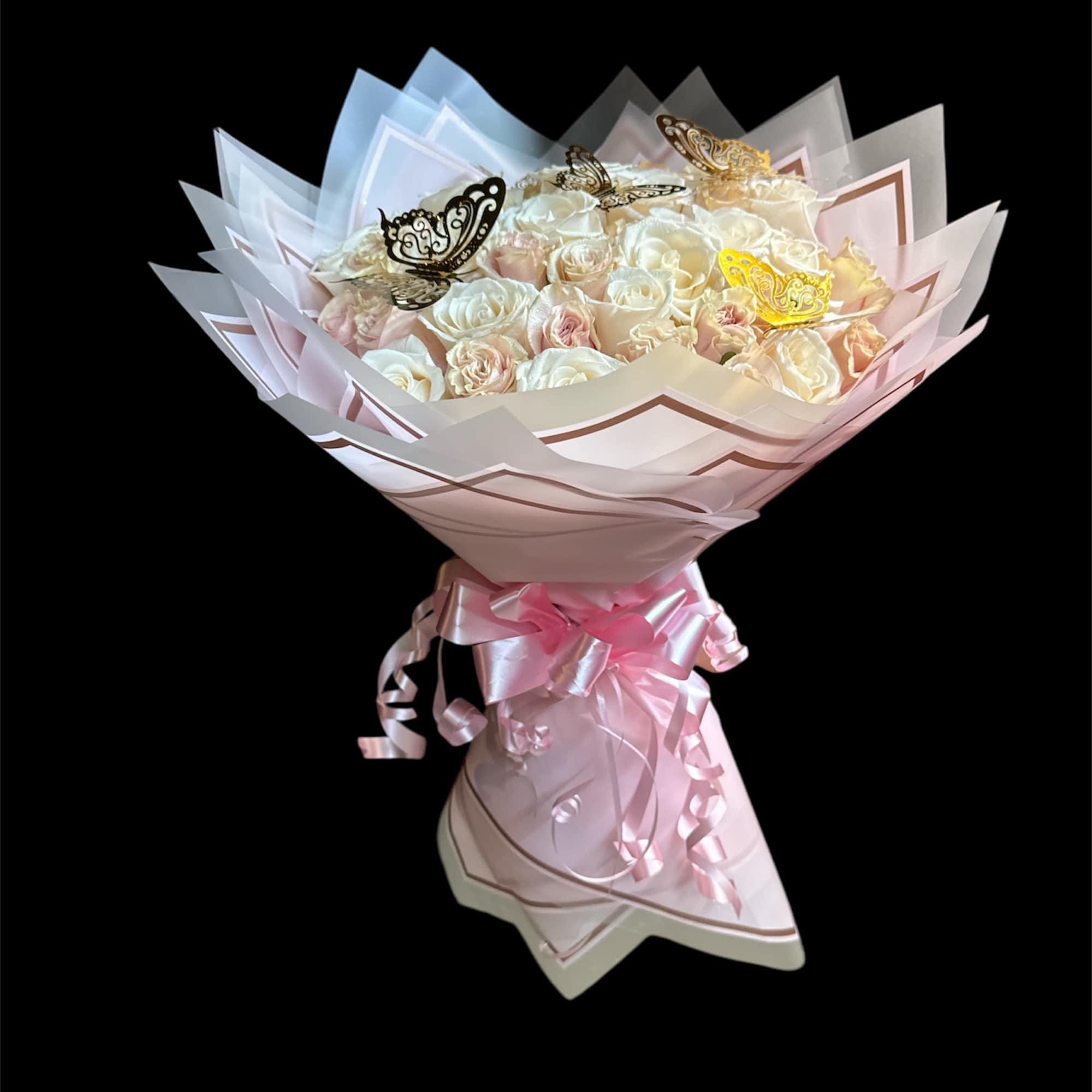 Bouquet of pale roses wrapped in pink paper with ribbon and butterfly picks