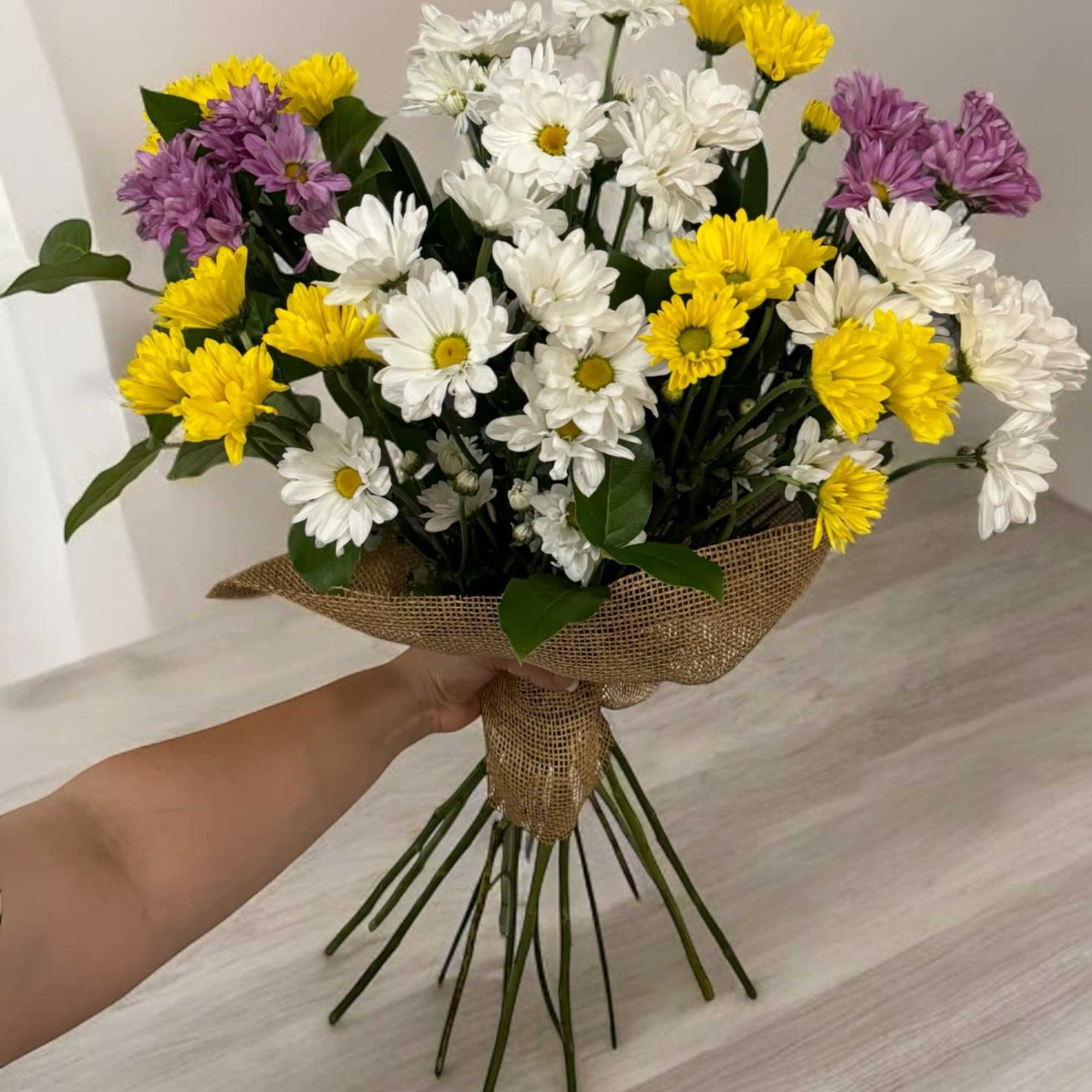 Bouquet of white, yellow, and purple daisies wrapped in burlap