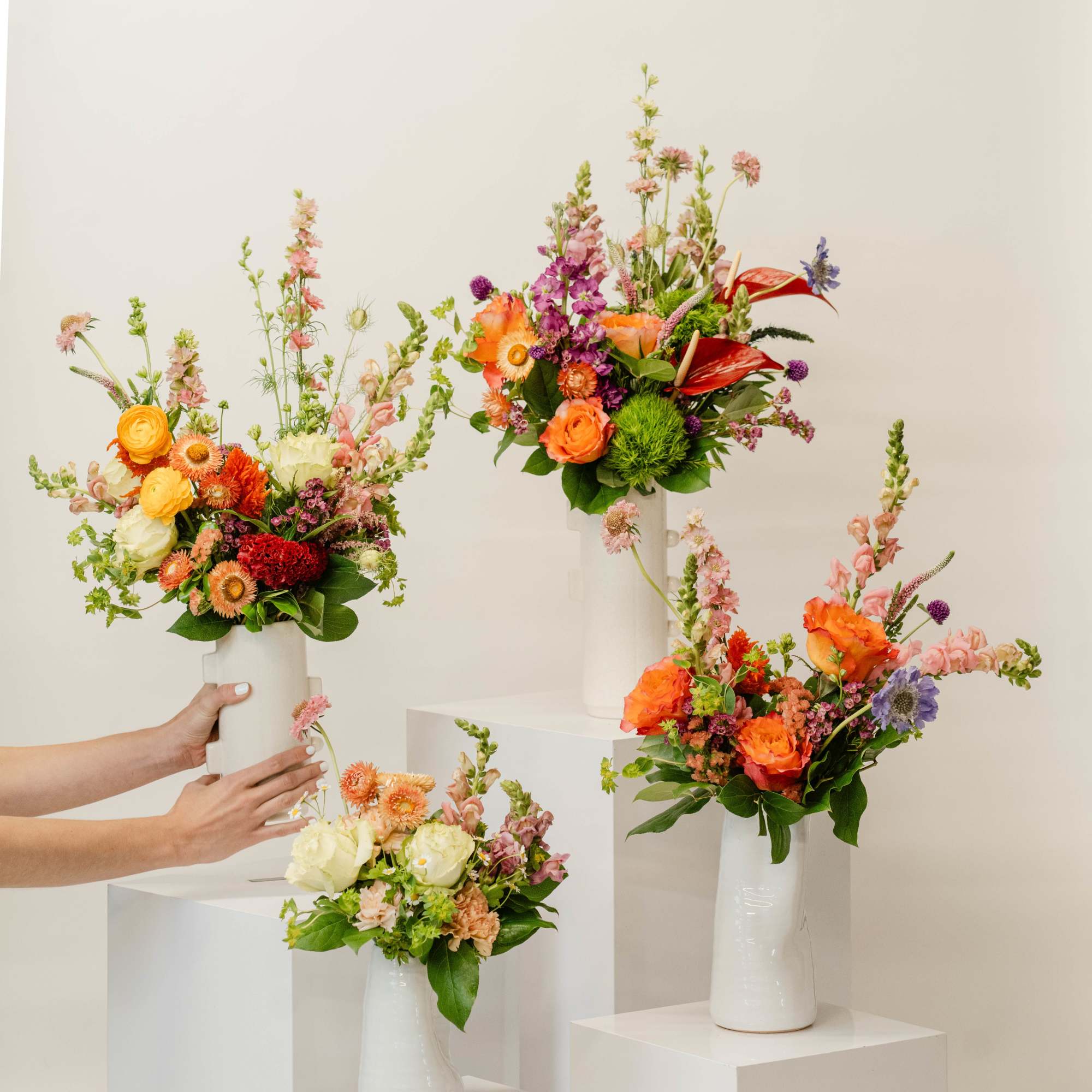Four colorful flower arrangements in white vases on pedestals