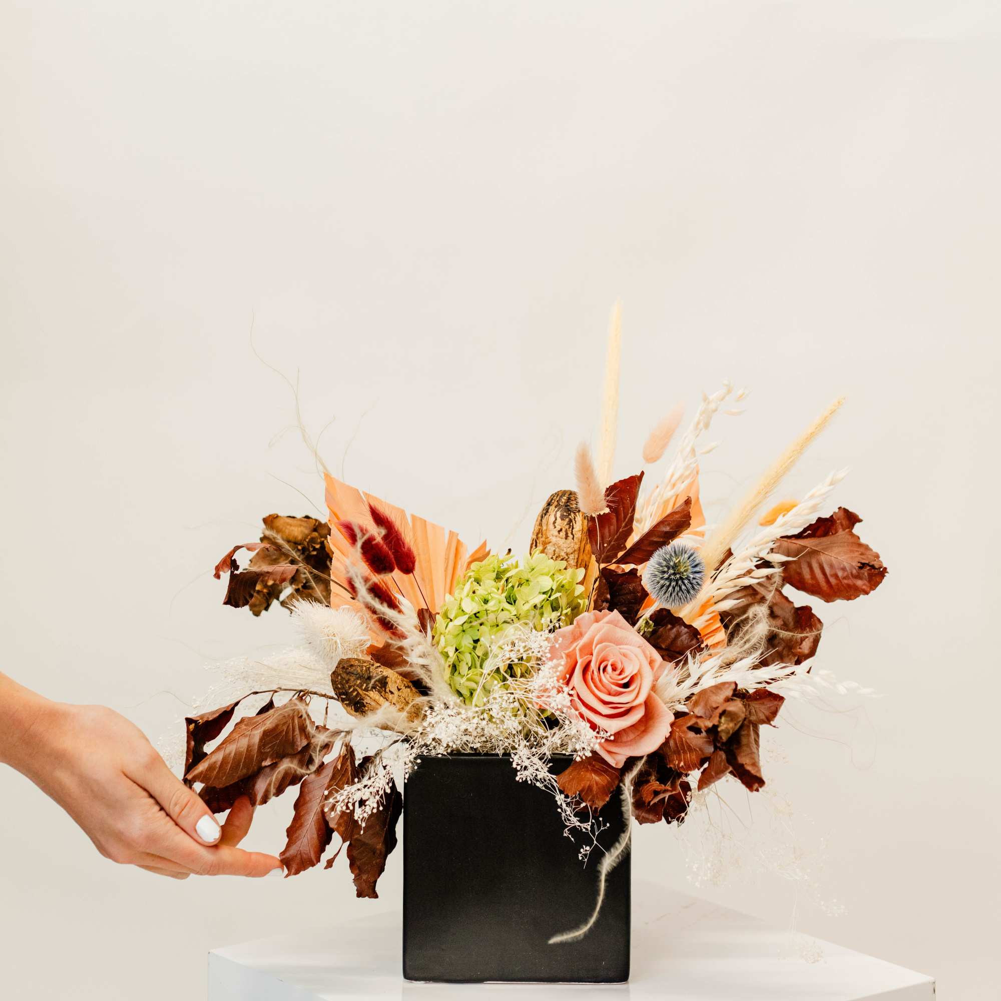 Arrangement of a peach rose and dried flowers in a black vase