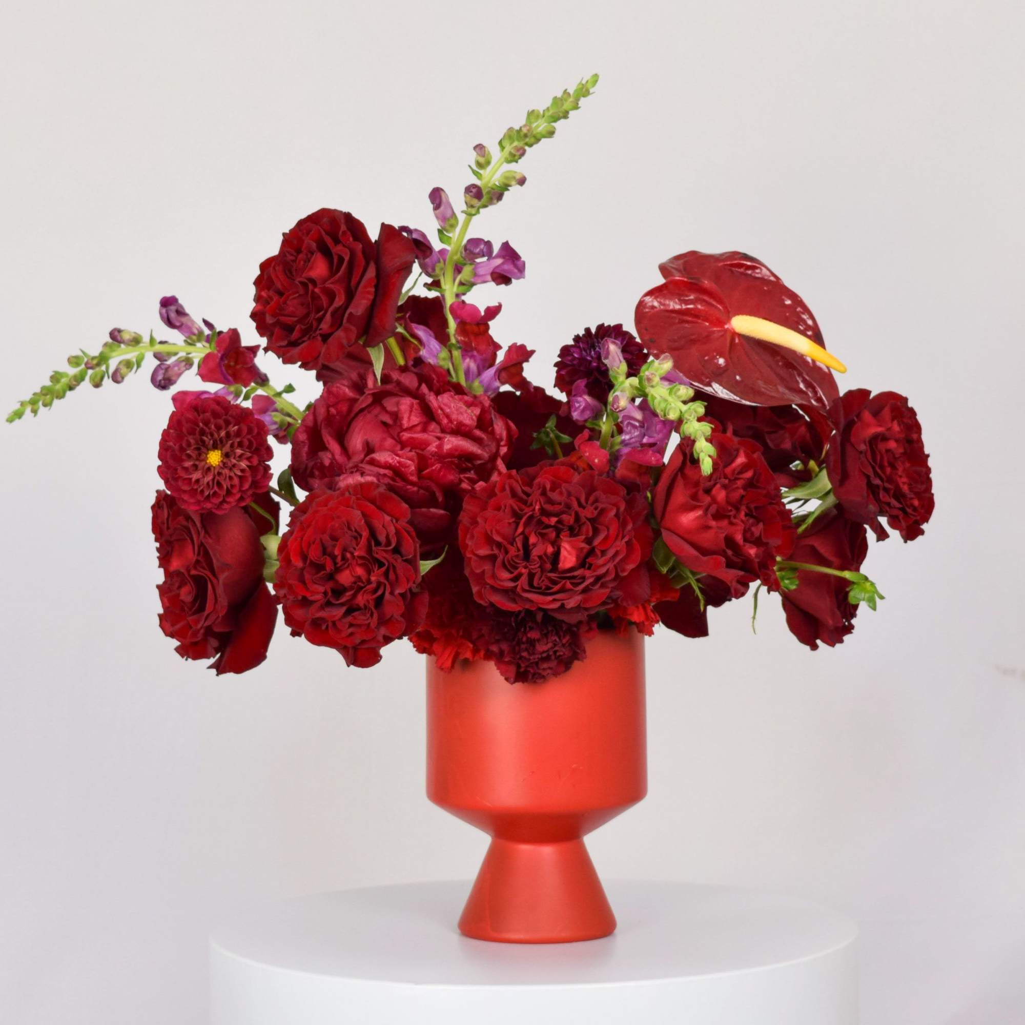 Red floral arrangement in a red vase with anthurium and roses