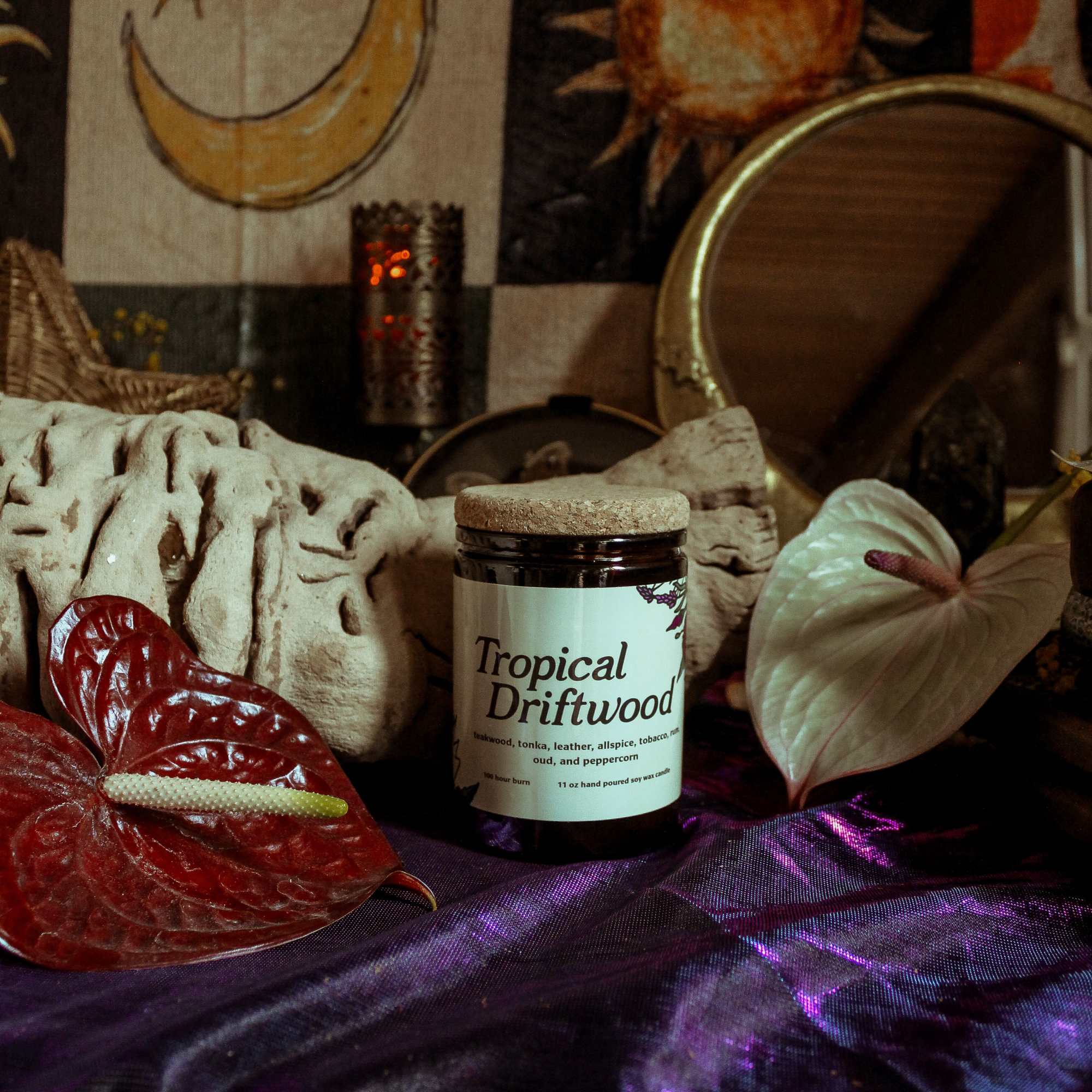 Jar candle with two anthurium blooms on a dark fabric surface