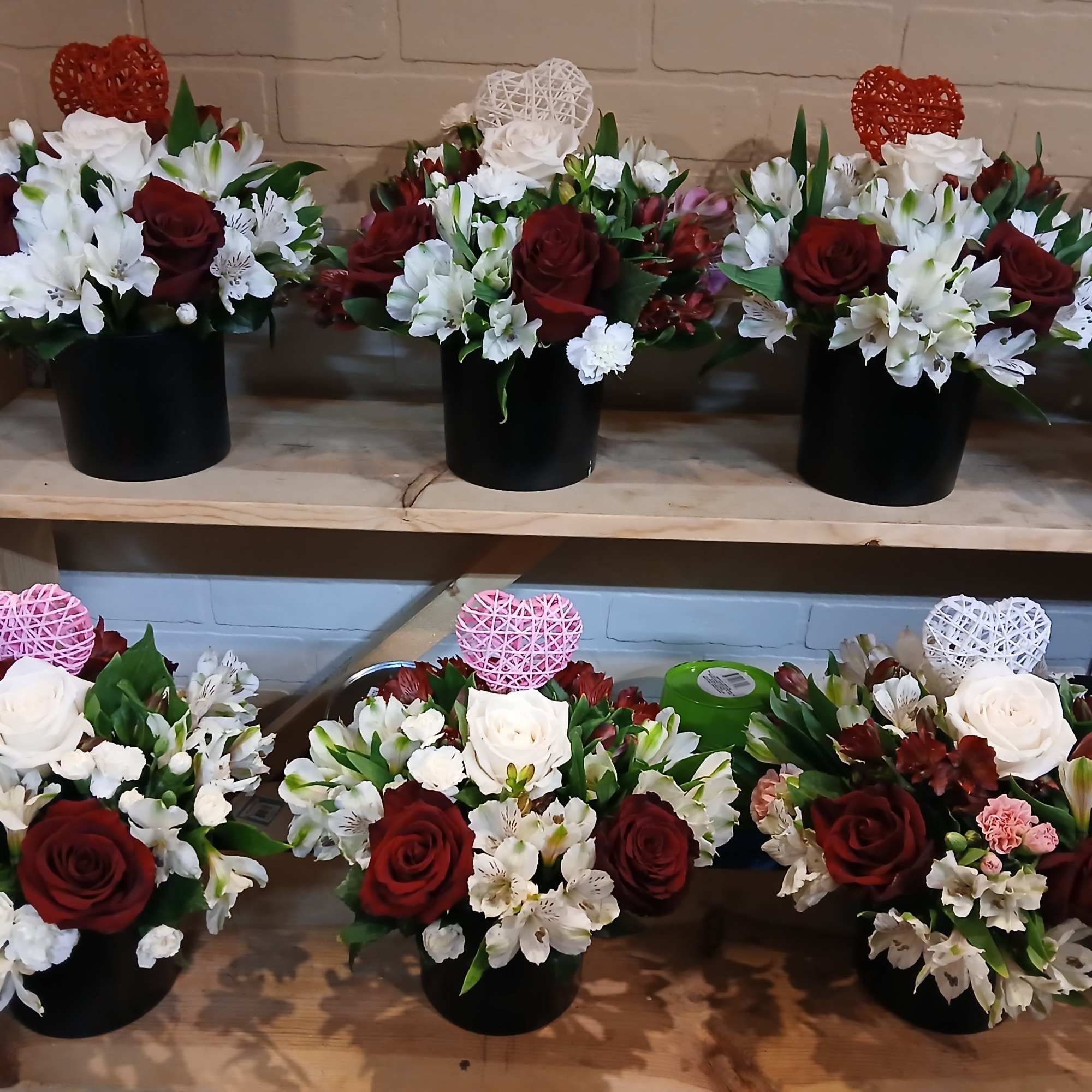 Several red and white floral arrangements in black containers on wooden shelves