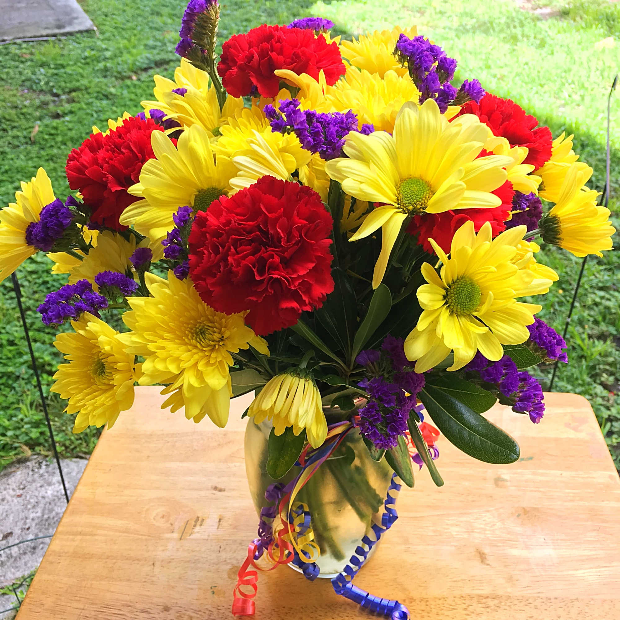 Red carnations, yellow daisies, purple Monte Casino blooms and green button poms