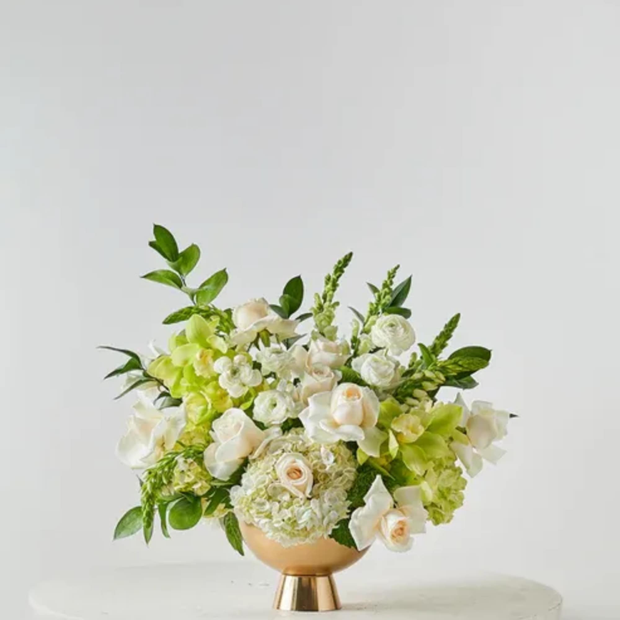 White and green floral arrangement in a gold pedestal vase