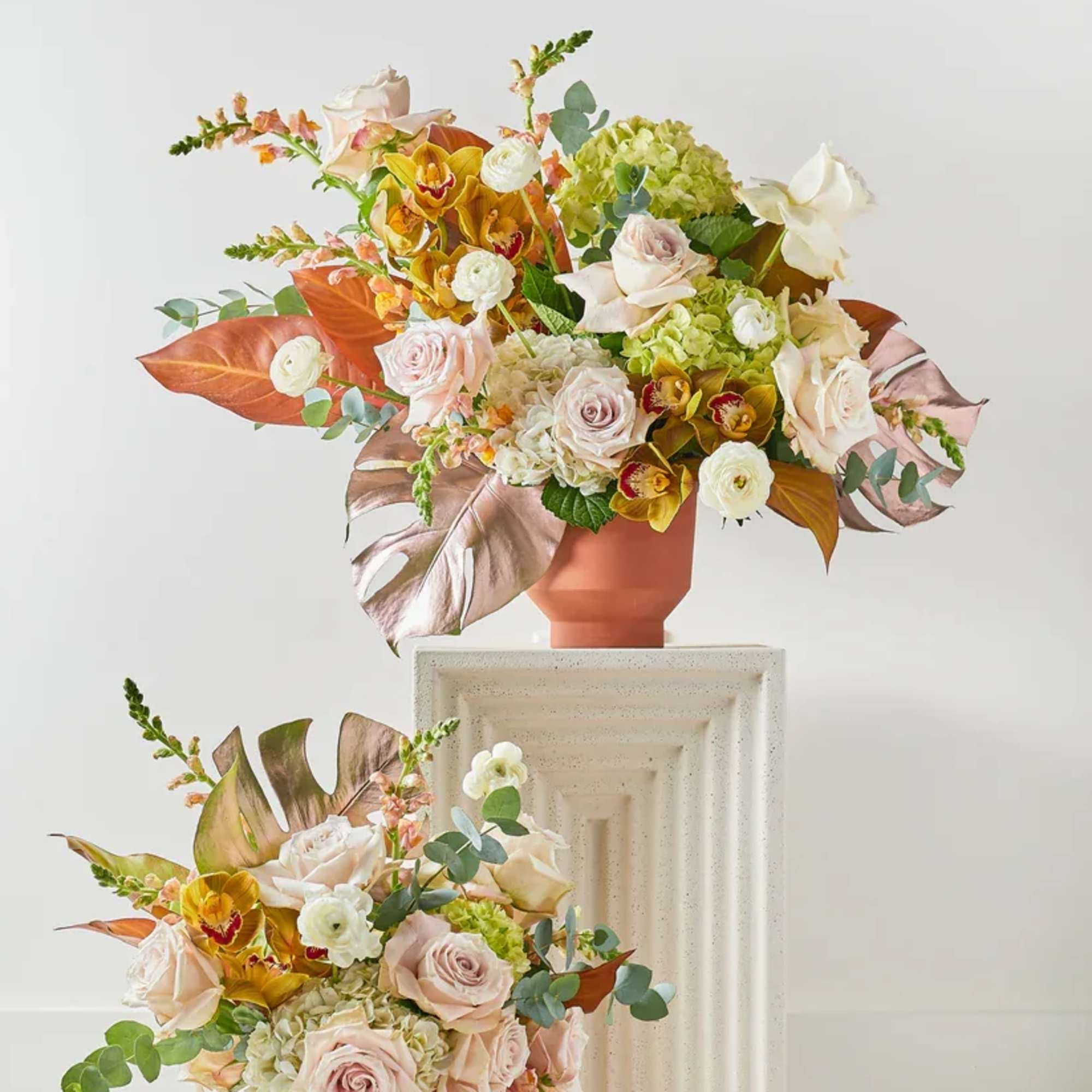 Two pastel floral arrangements in terracotta vases on pedestals