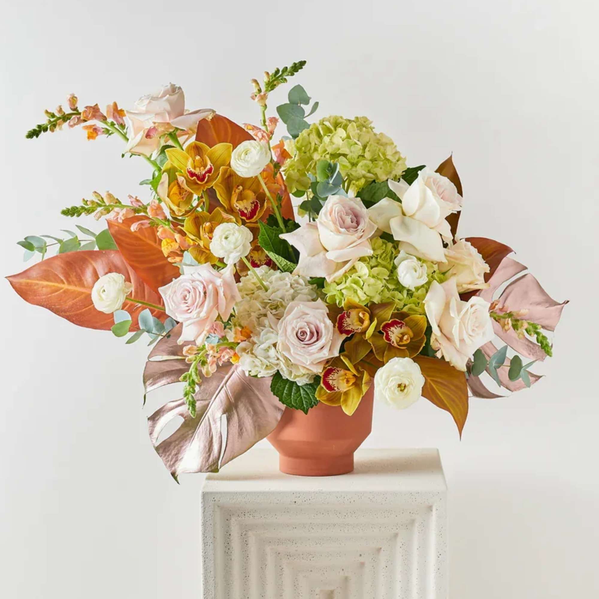 Mixed floral arrangement in a terracotta vase with pale roses and green hydrangea