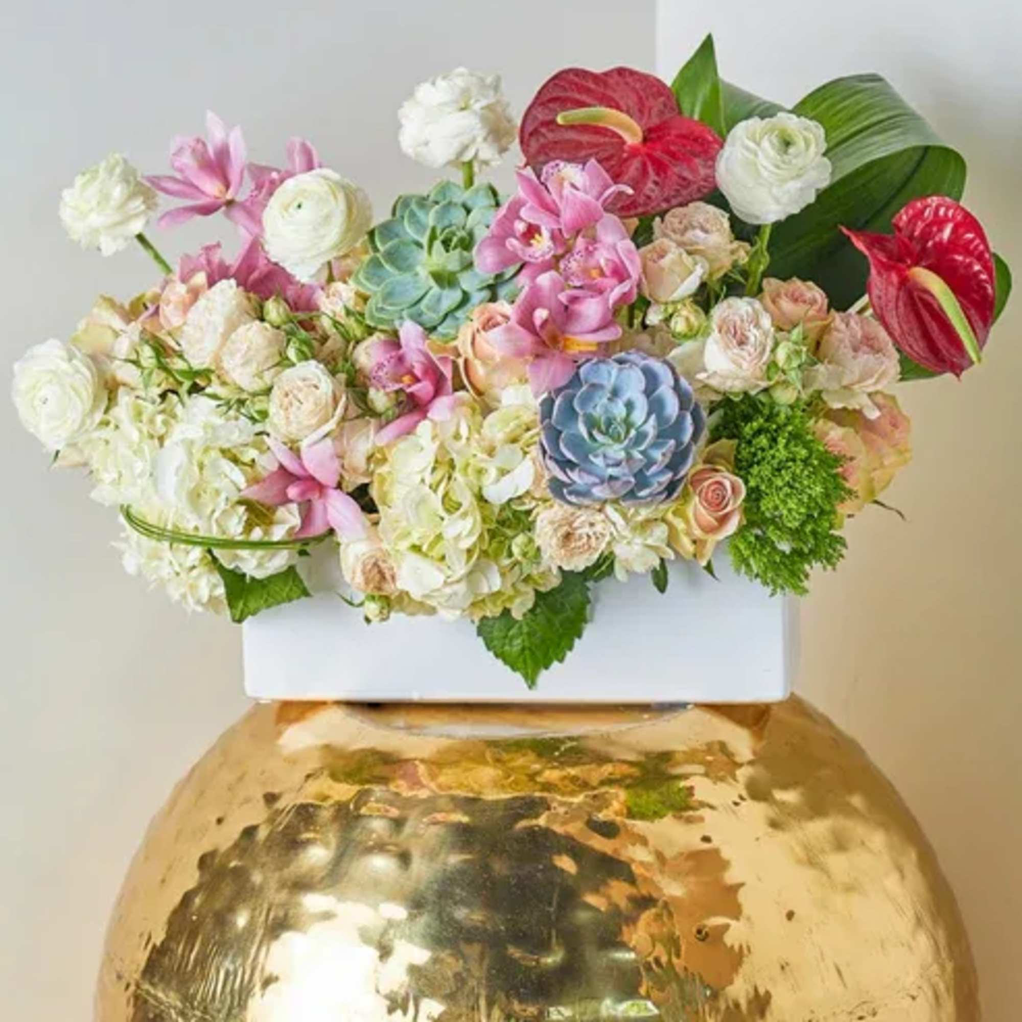 Mixed floral arrangement in a white container on a gold vase