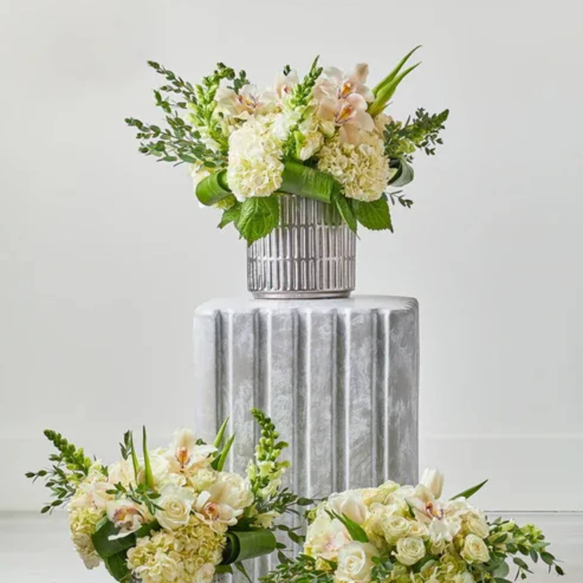 Three white floral arrangements in ribbed silver vases on pedestals