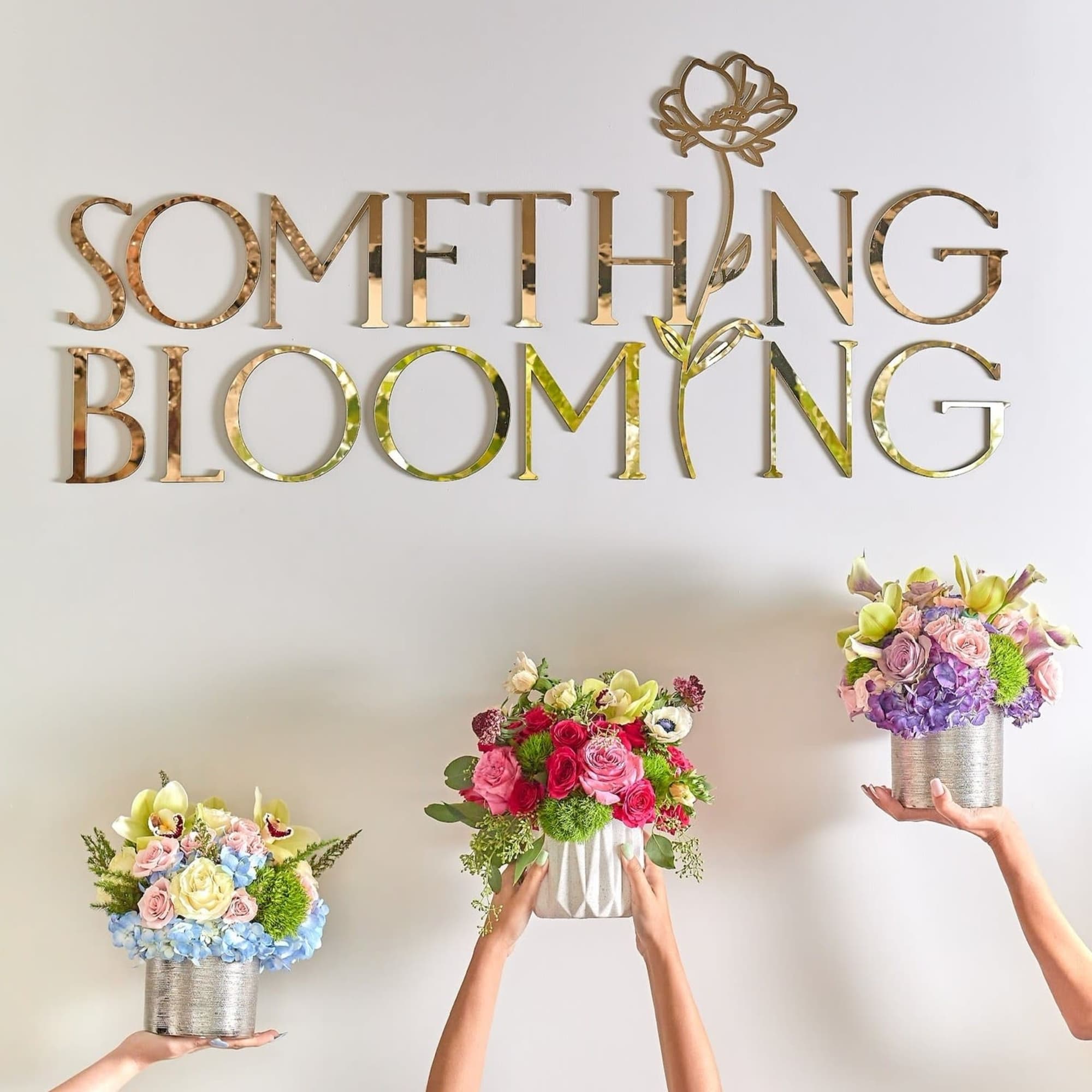 Three colorful floral arrangements held up against a wall with gold lettering