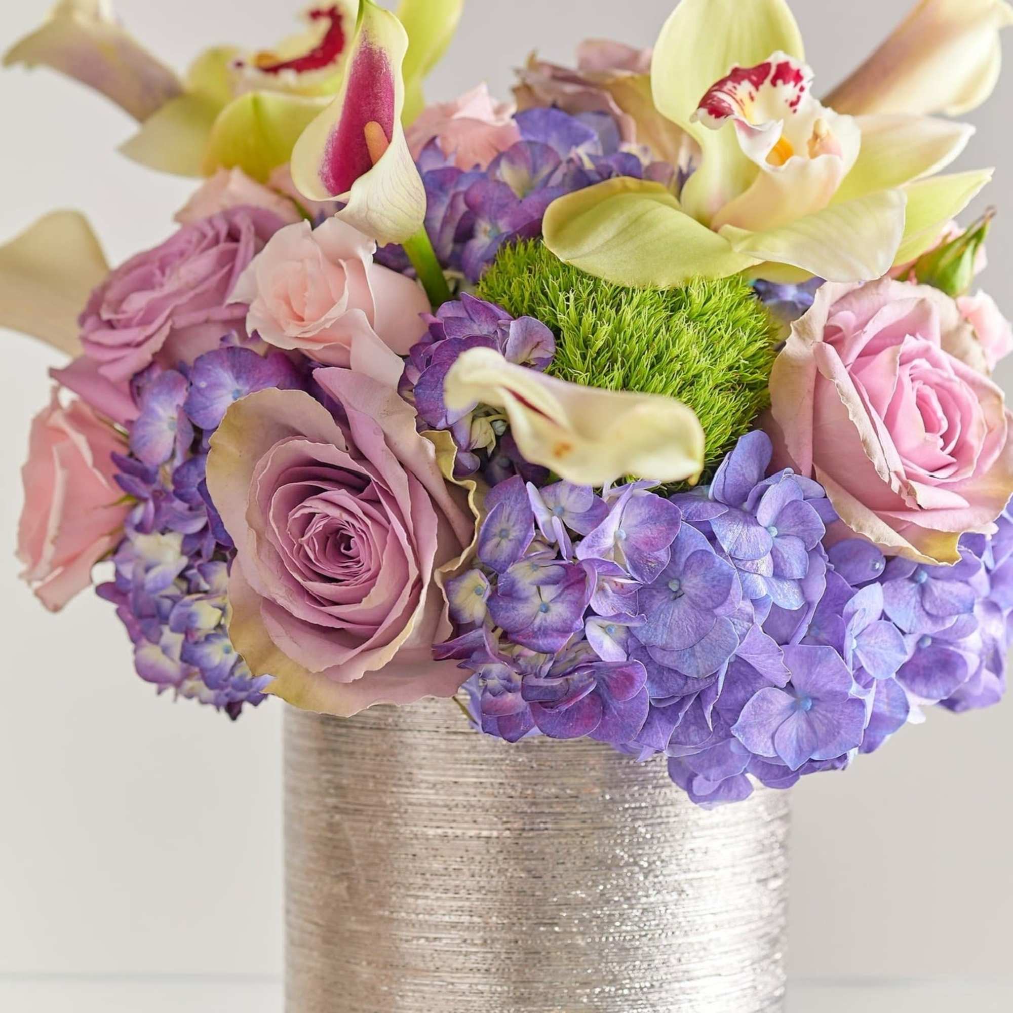 Bouquet of pink roses, purple hydrangeas, and pale orchids in a silver vase
