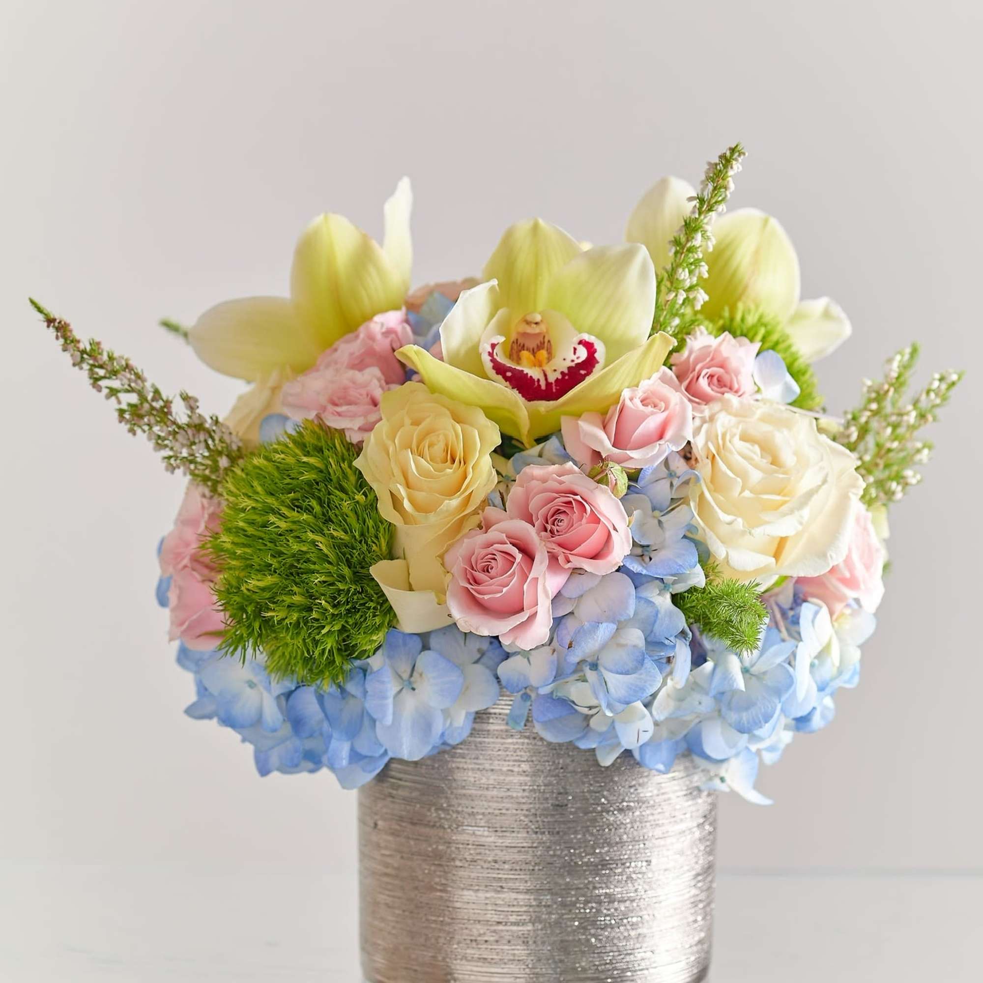 Pastel flower arrangement in a silver vase with roses, orchids, and hydrangeas