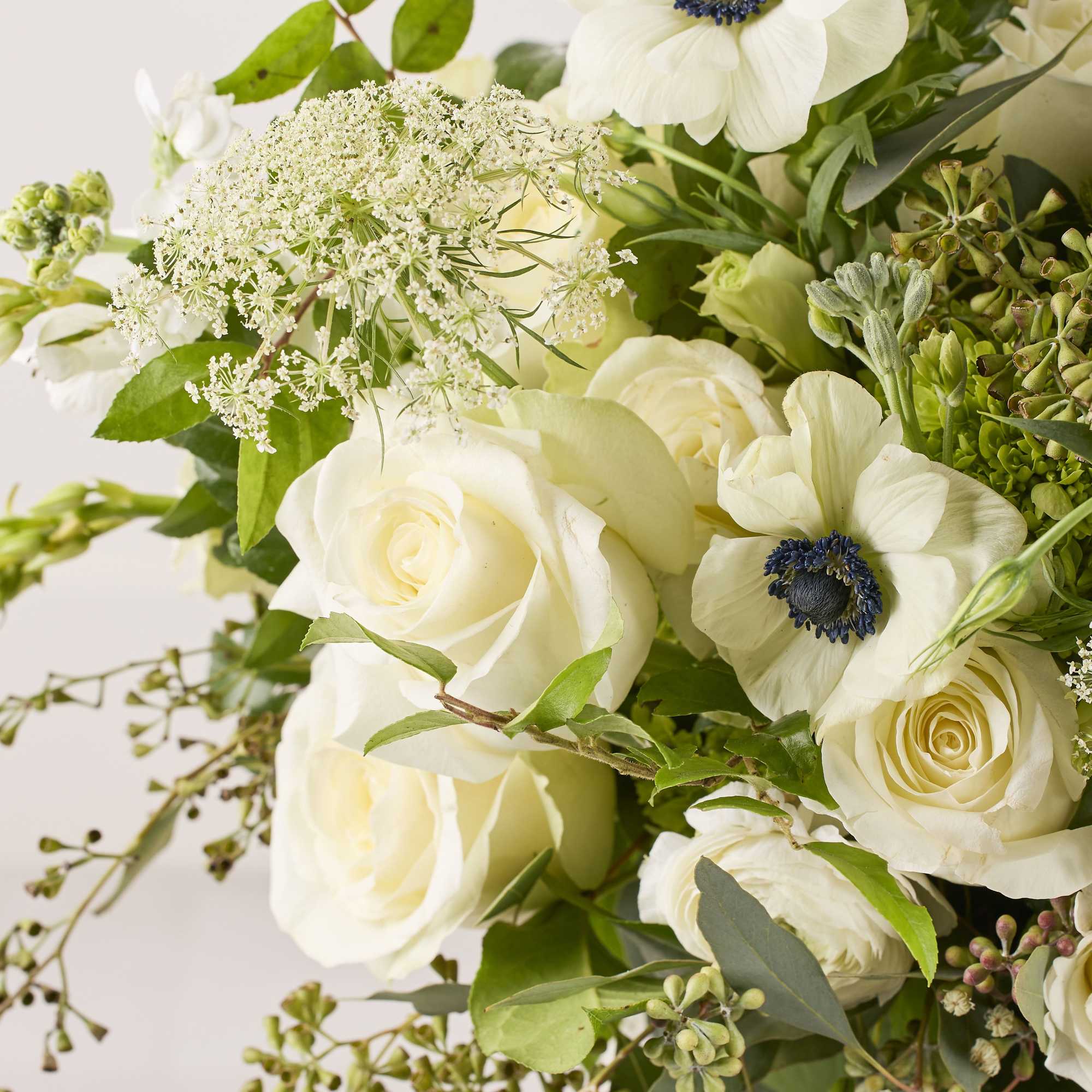 White roses and anemones in a loose bouquet with greenery