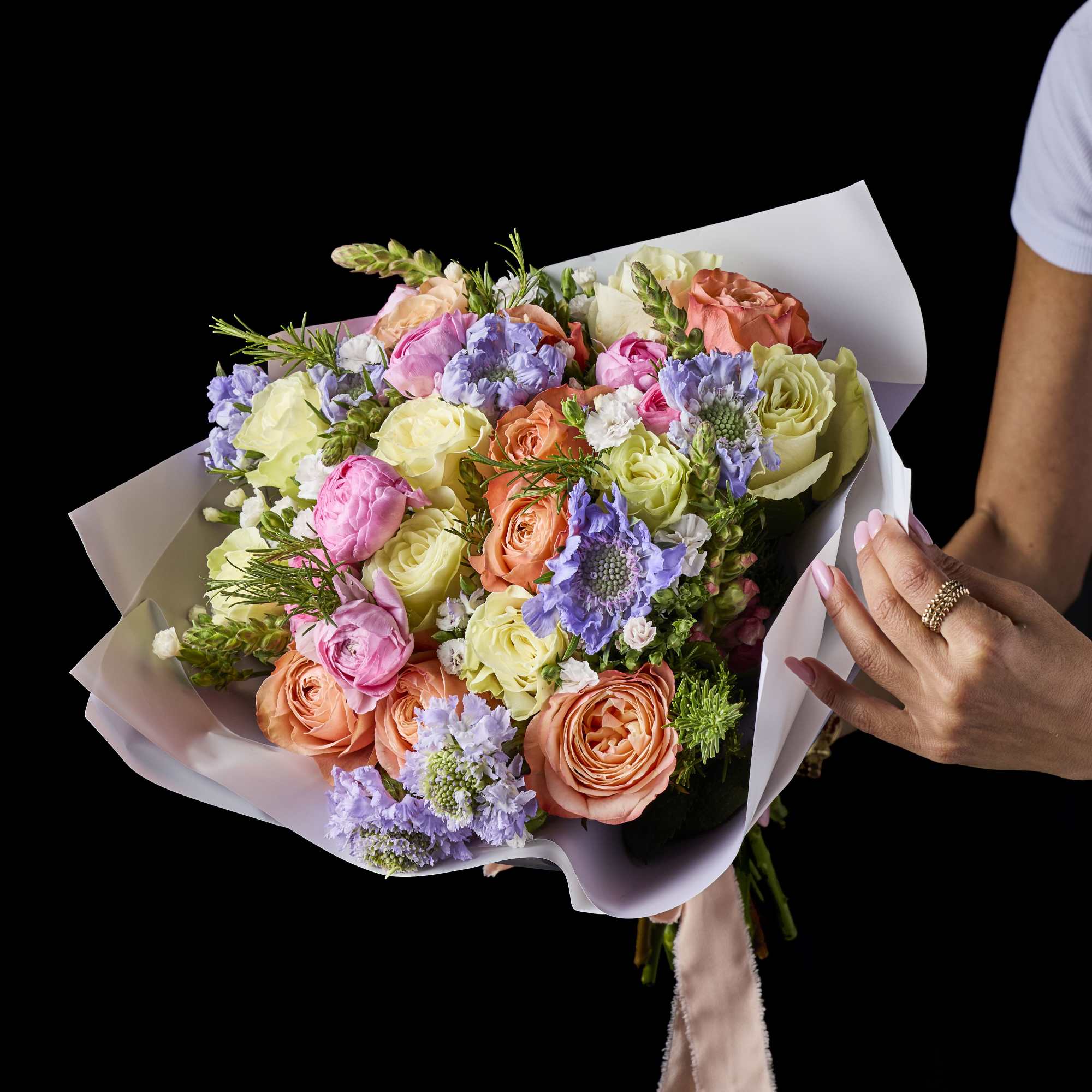 Hand-tied bouquet of pastel roses and purple blooms in white wrap