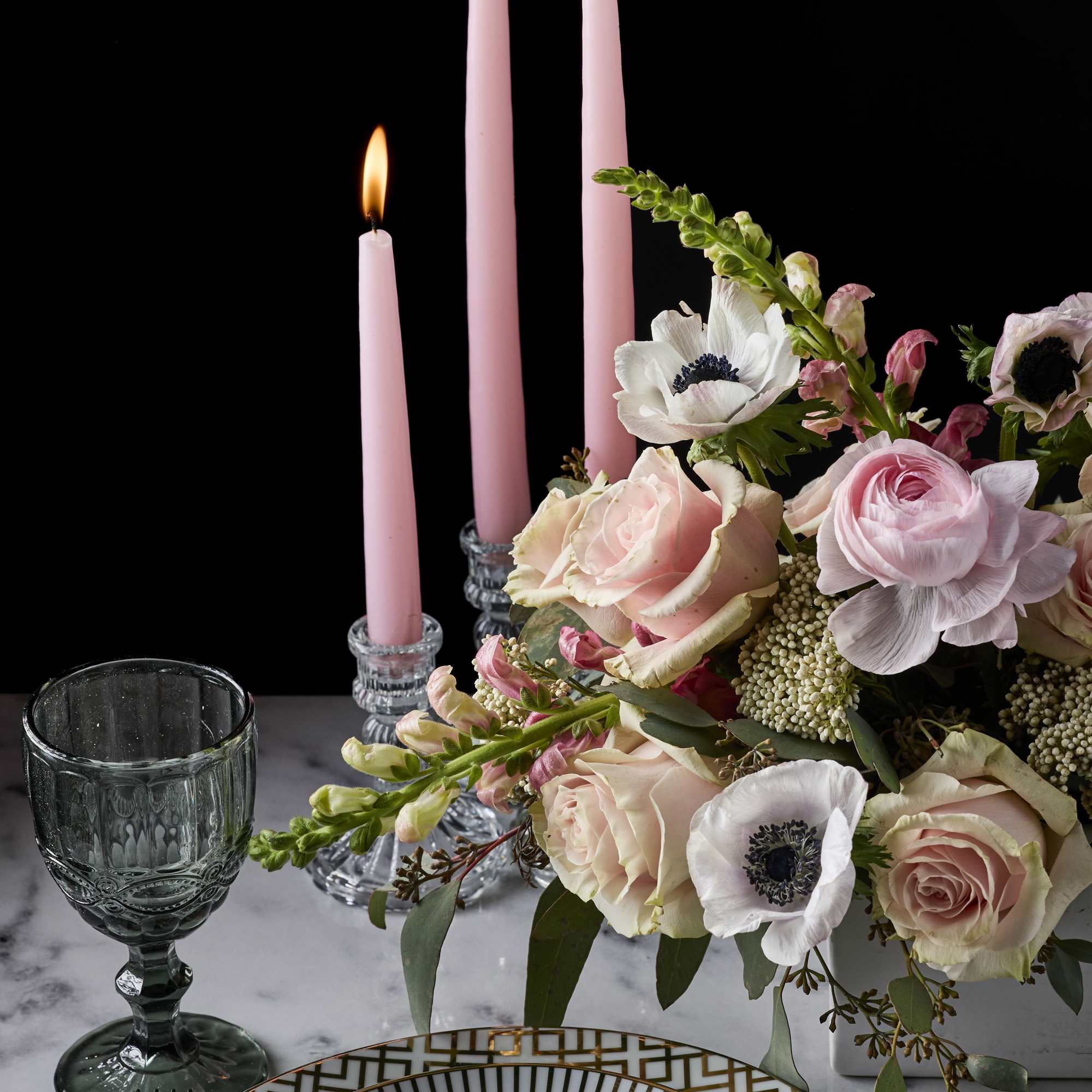 Pink candles beside a pastel floral centerpiece on a table setting