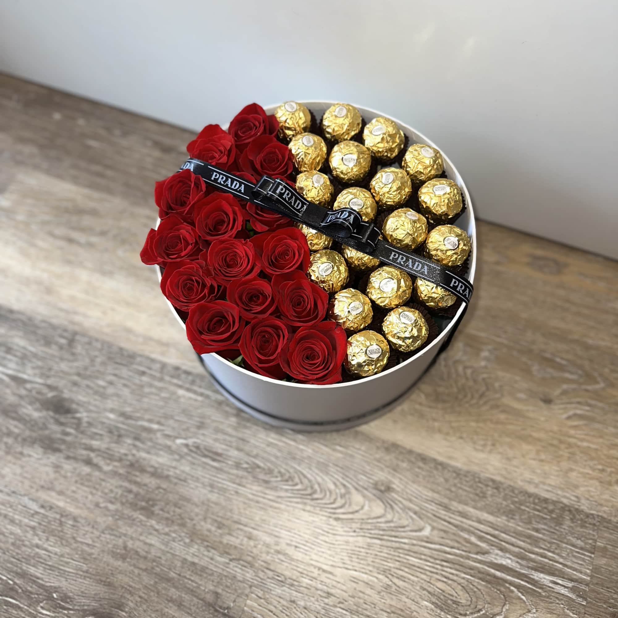 Red roses and gold-wrapped chocolates arranged in a round white box