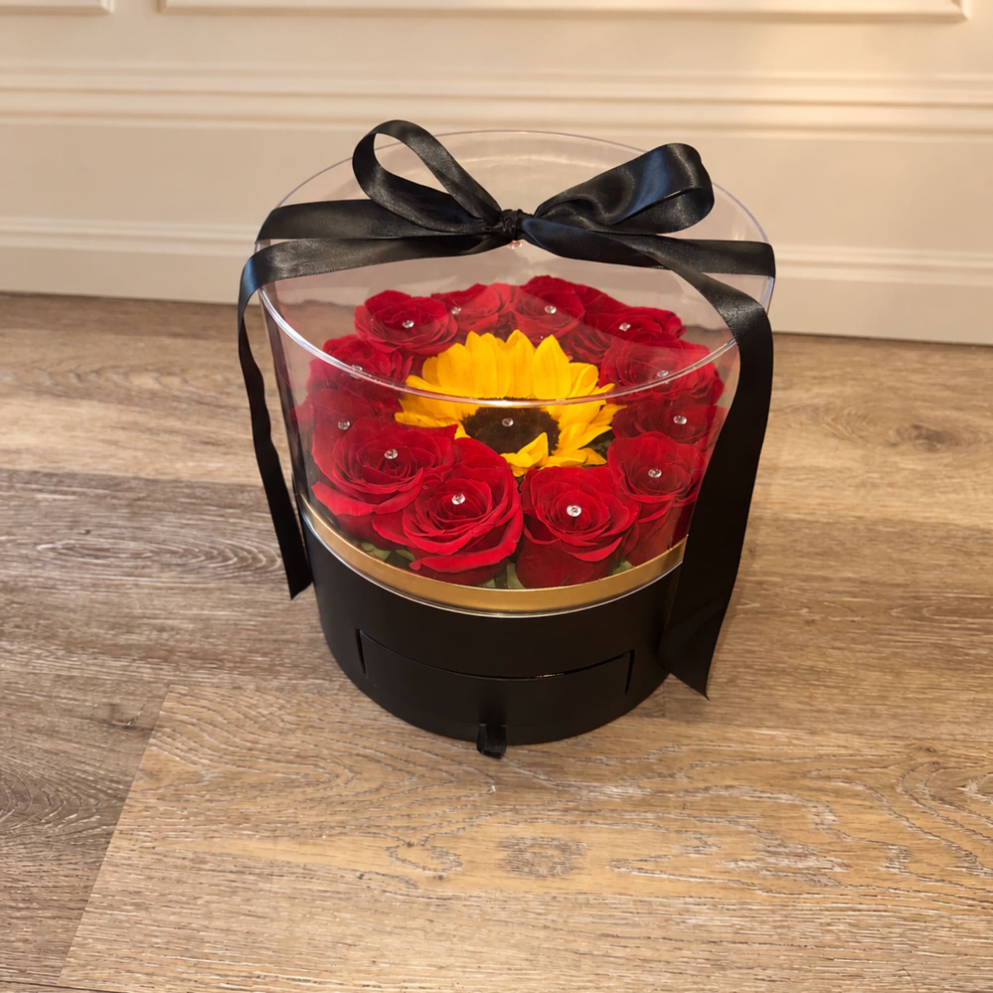 Red roses and a yellow sunflower in a black gift box with a clear lid and ribbon