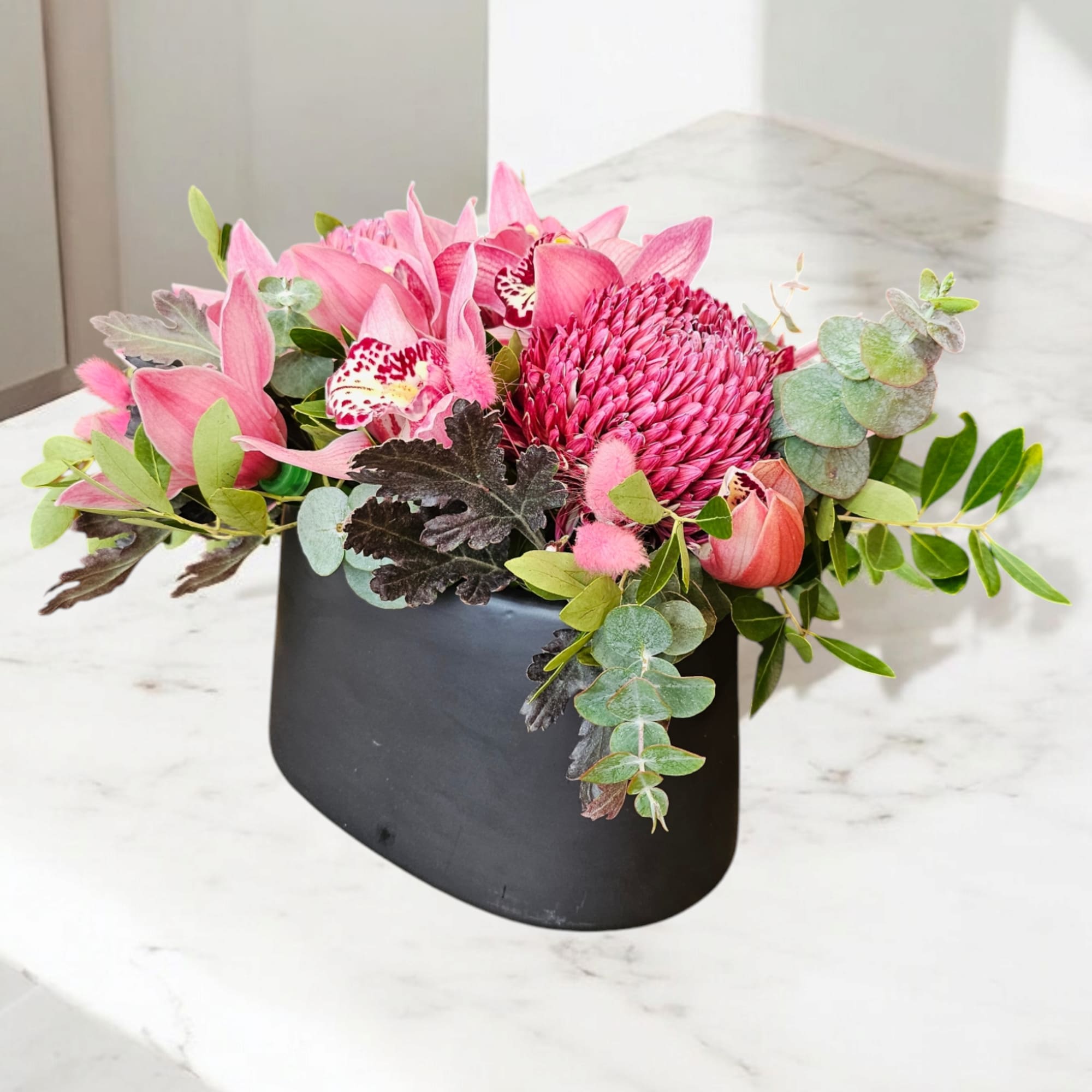 Pink floral arrangement in a black container with eucalyptus and orchids