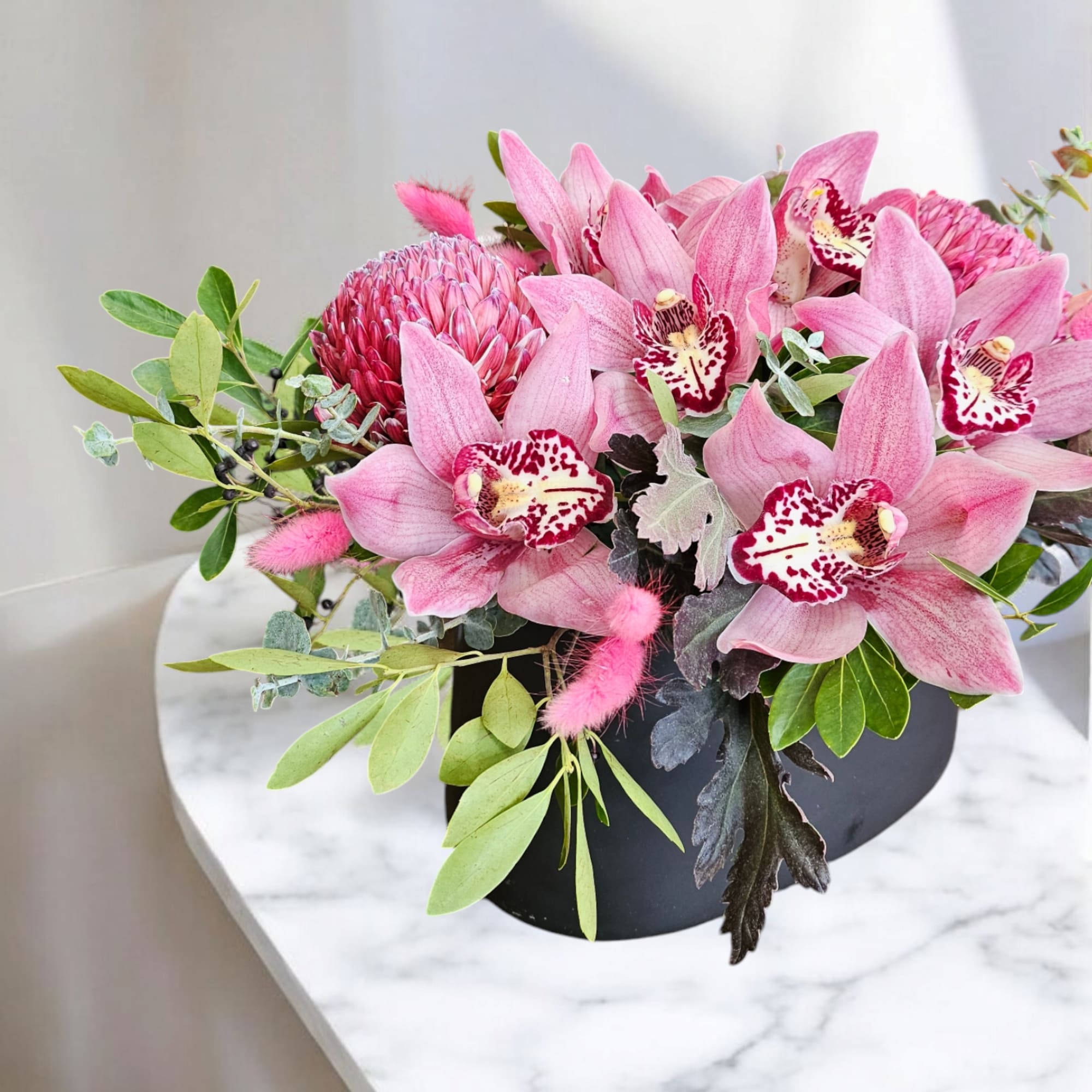 Pink orchids and protea arranged in a black bowl vase