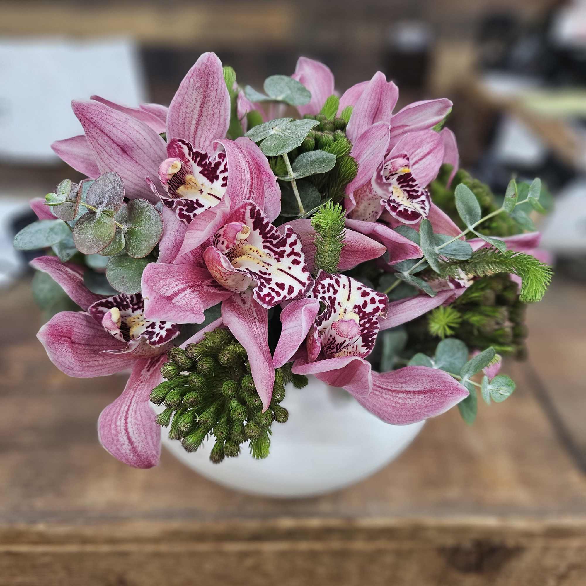 Pink orchids arranged in a white vase with eucalyptus