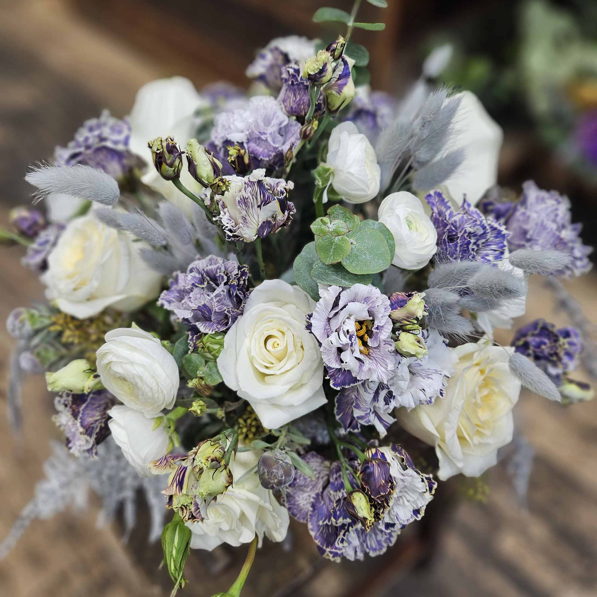 Hand-tied bouquet of white roses and ranunculus with purple lisianthus and soft gray accents.