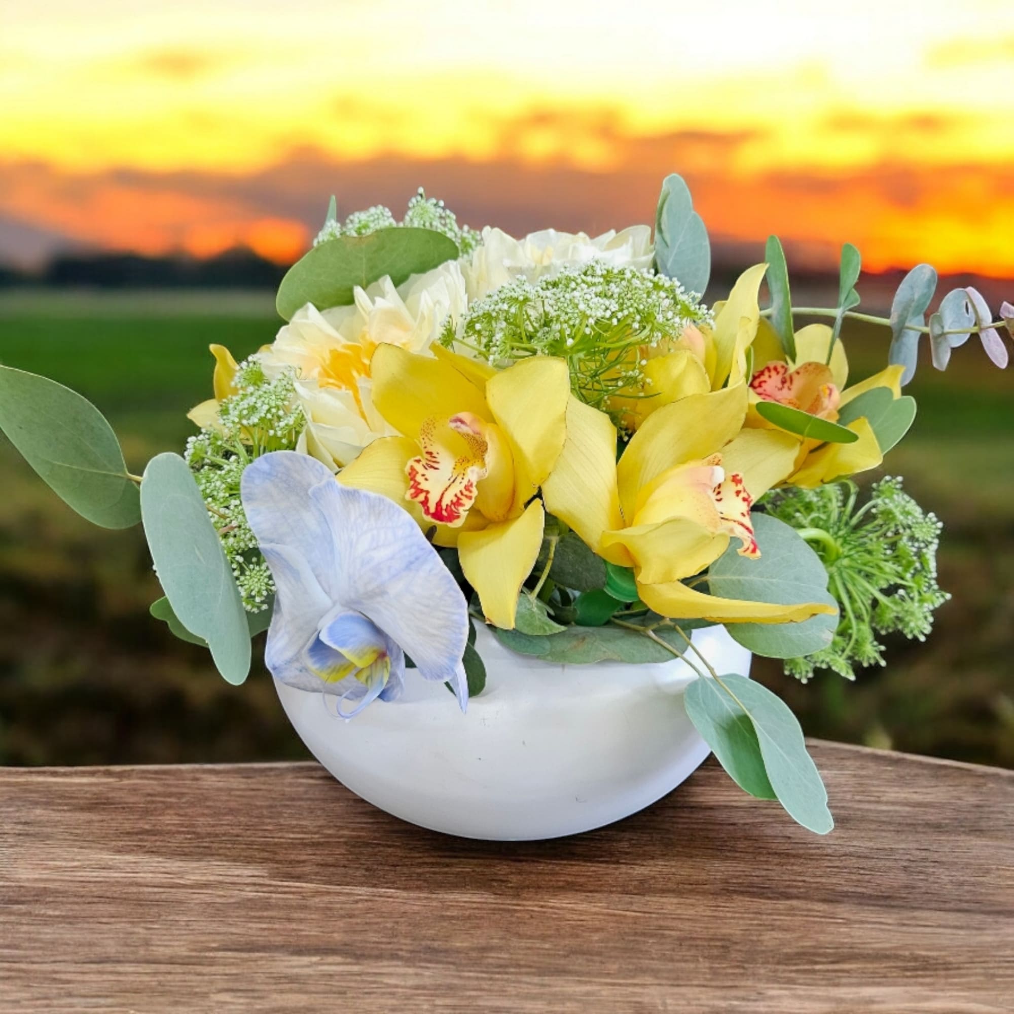 Yellow and pale blue orchids in a white bowl vase
