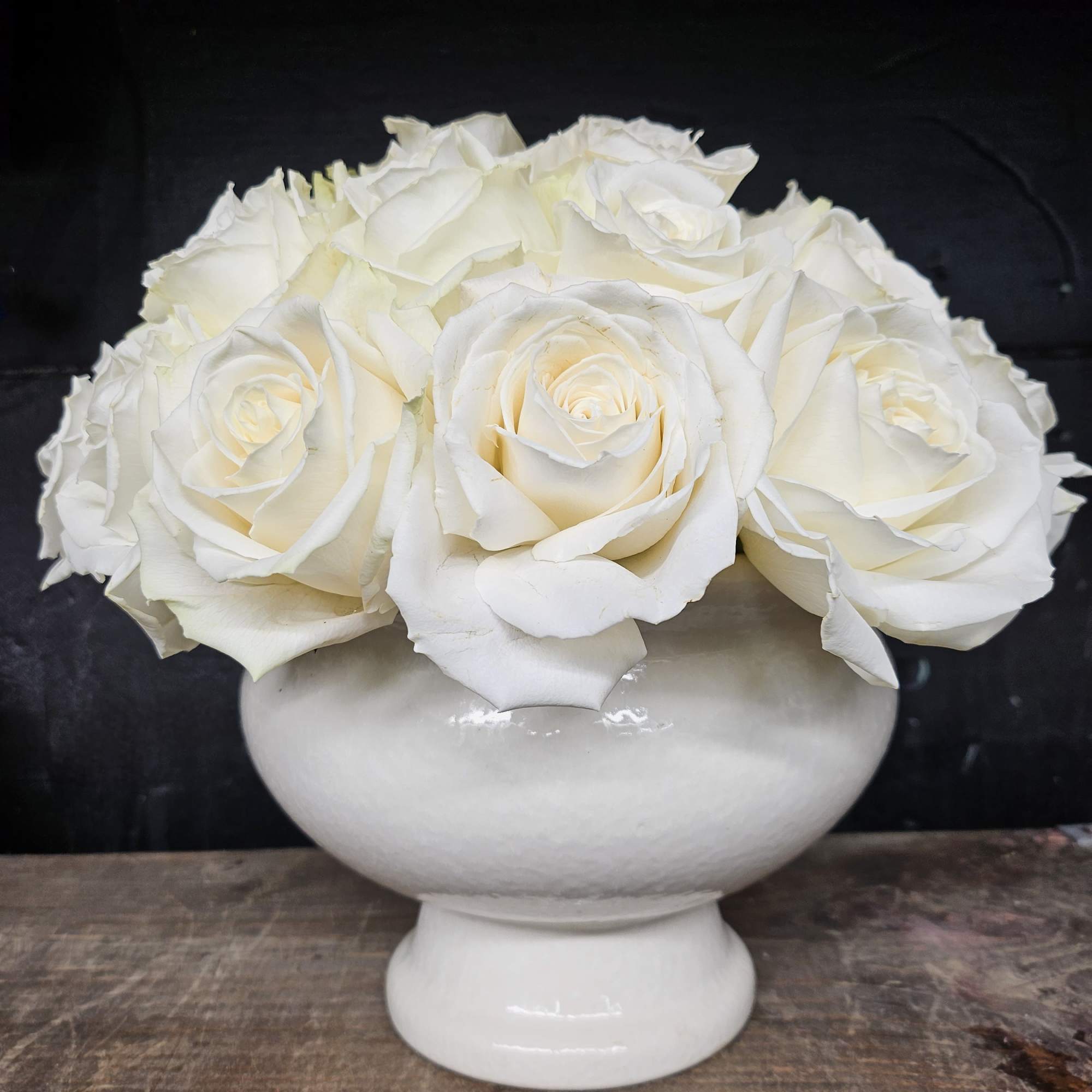 White roses arranged in a white pedestal vase