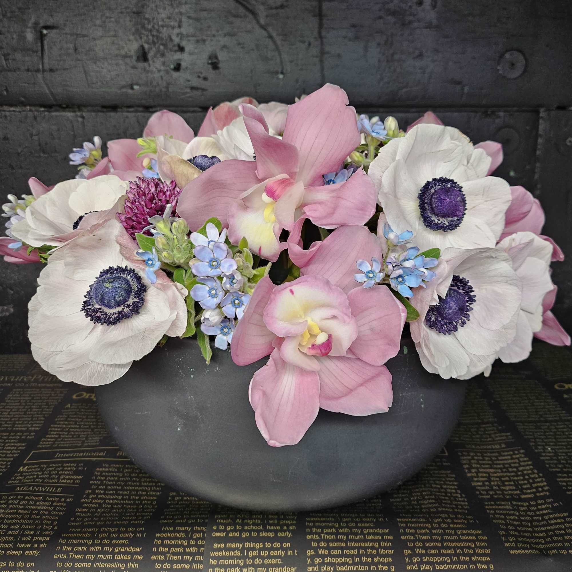 Pink orchids and white anemones arranged in a low black bowl
