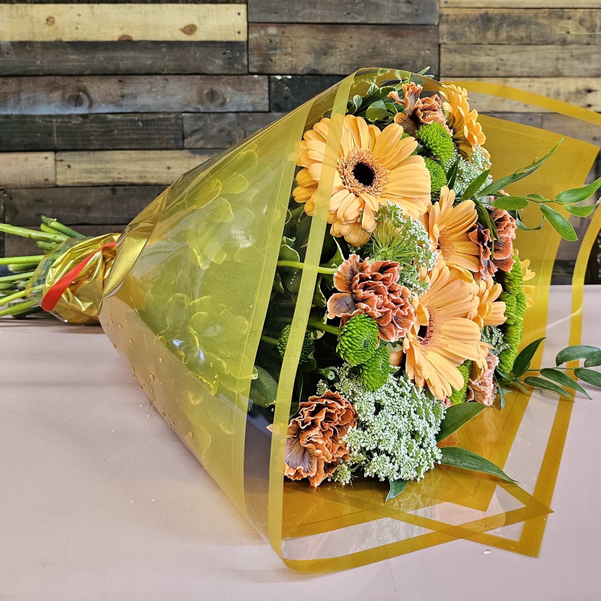Bouquet of orange gerbera daisies and carnations wrapped in yellow cellophane