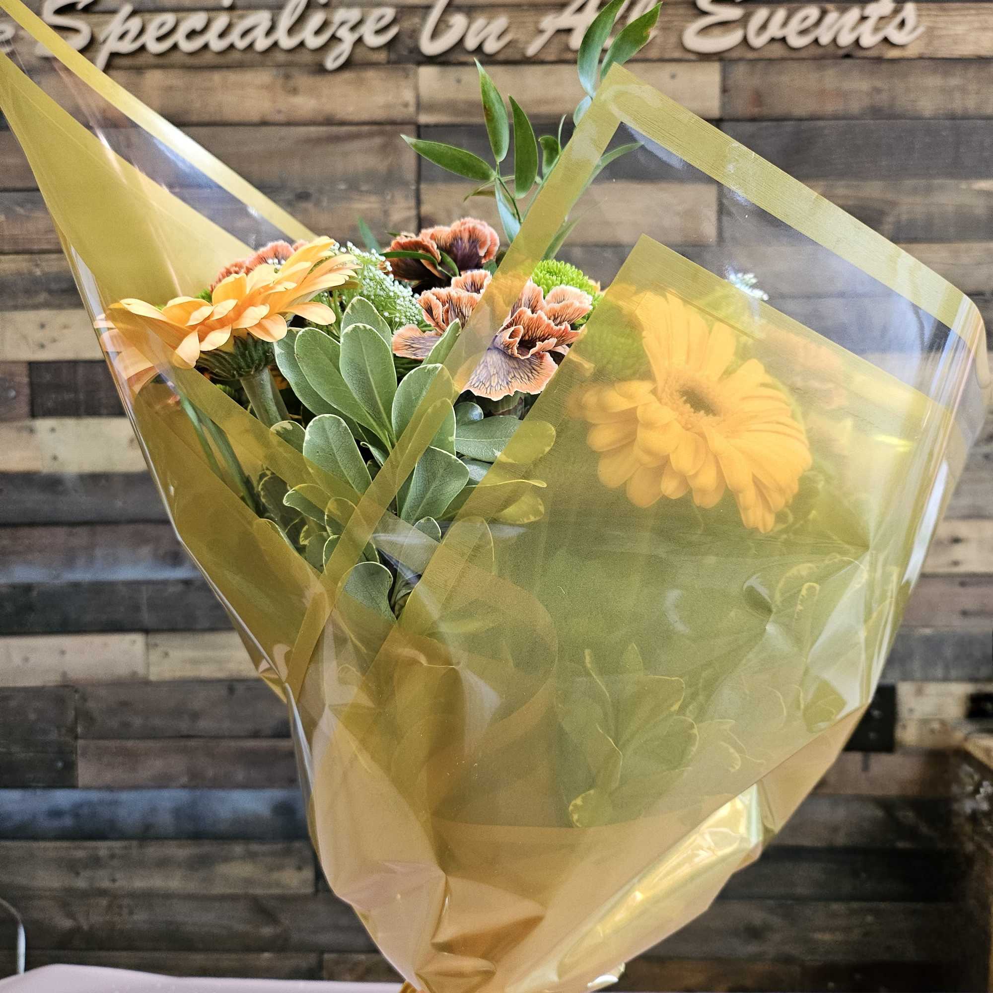Wrapped bouquet of orange and peach flowers with green foliage