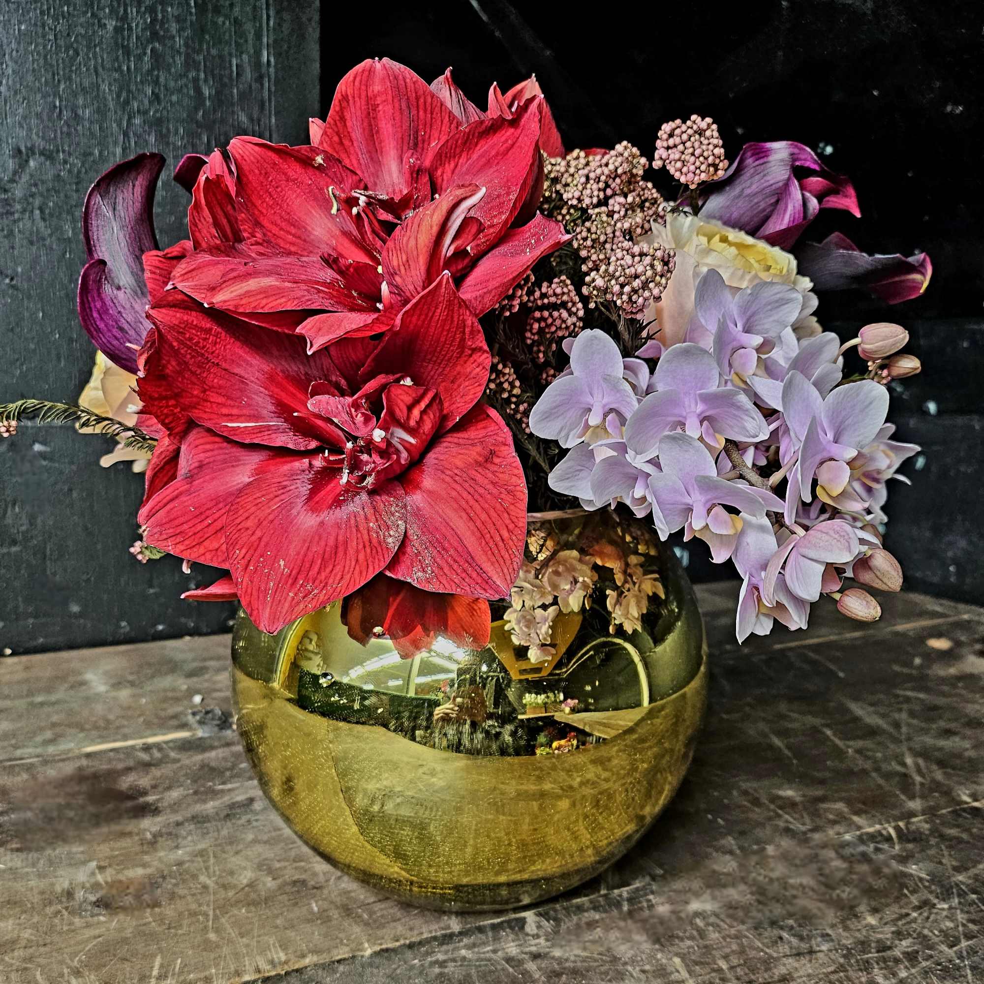 Red amaryllis and pale purple orchids in a gold vase