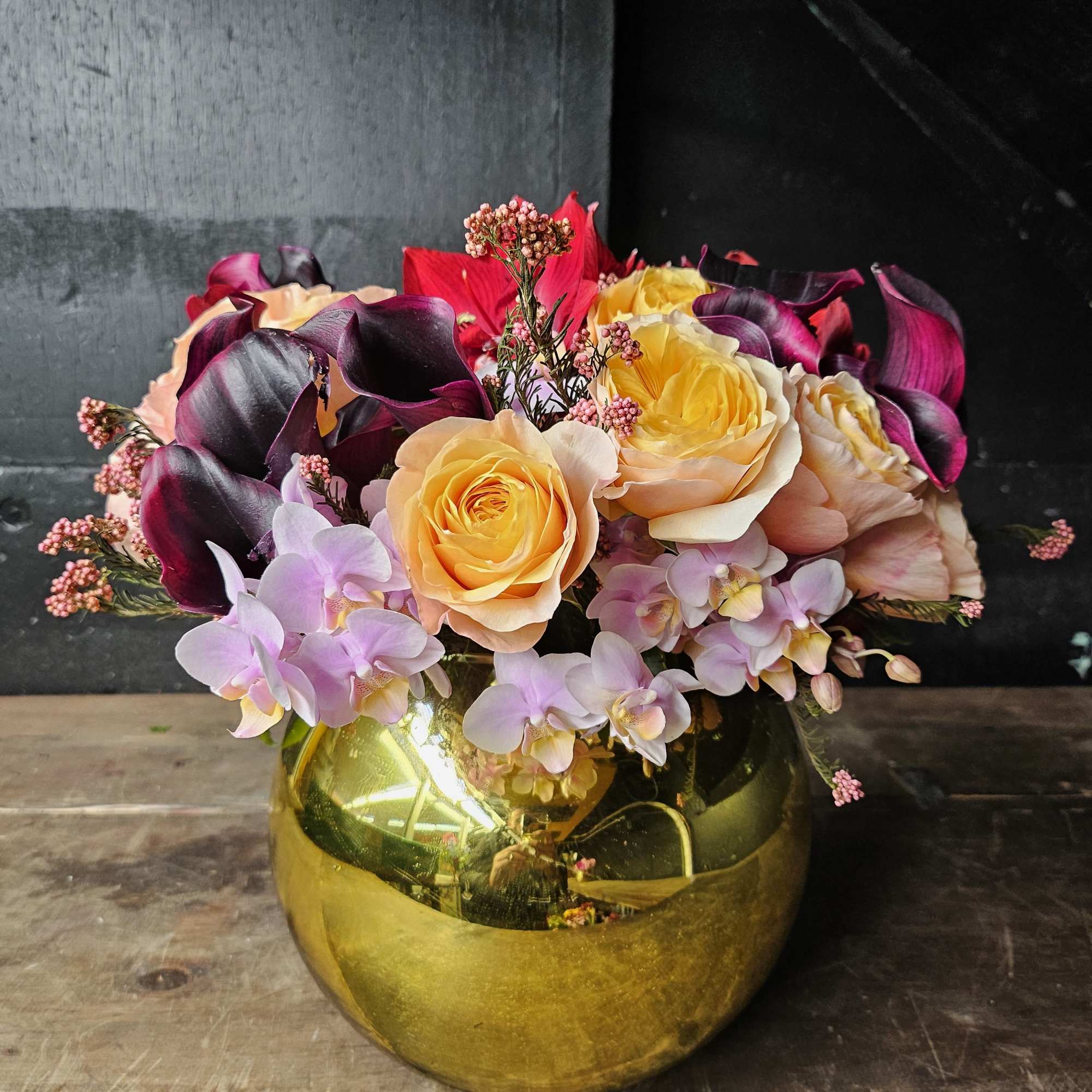 Bouquet of yellow roses, purple calla lilies, and pale orchids in a gold vase