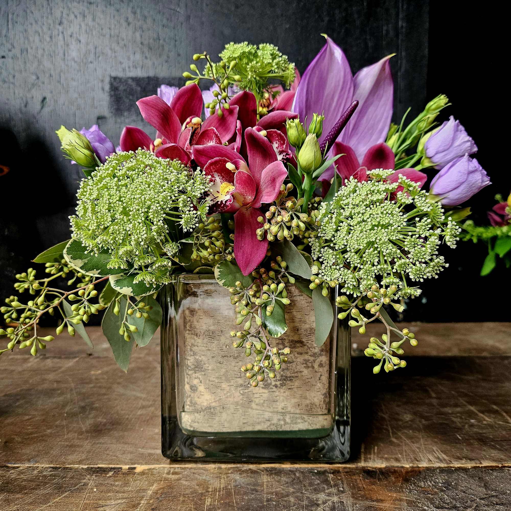 Pink and purple flowers arranged in a square glass vase