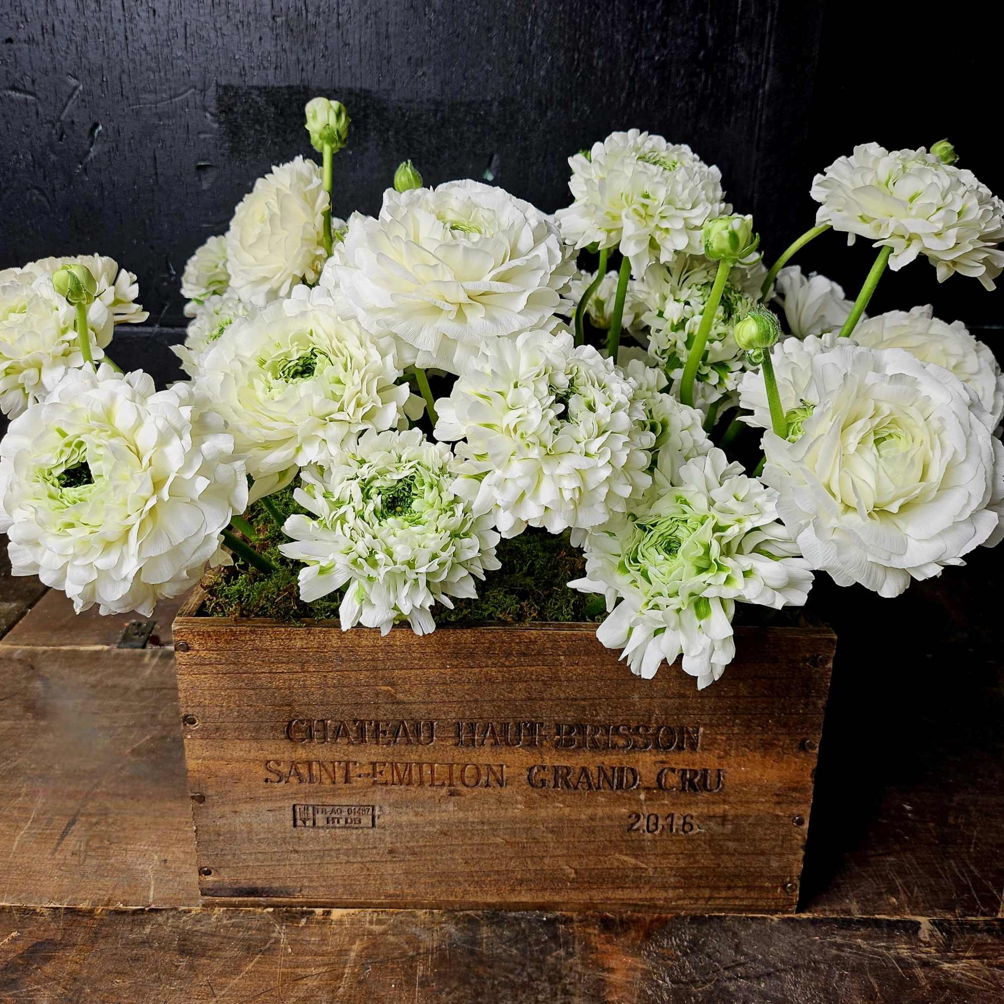 White ranunculus and pompom blooms in a wooden crate