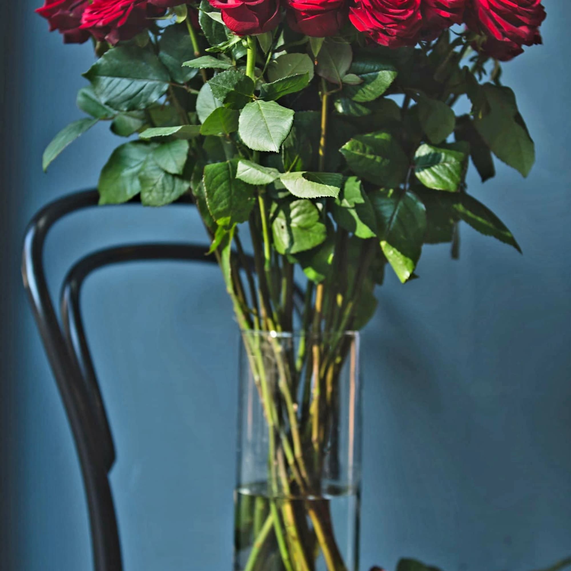 Red roses in a clear glass vase with a few roses on the table