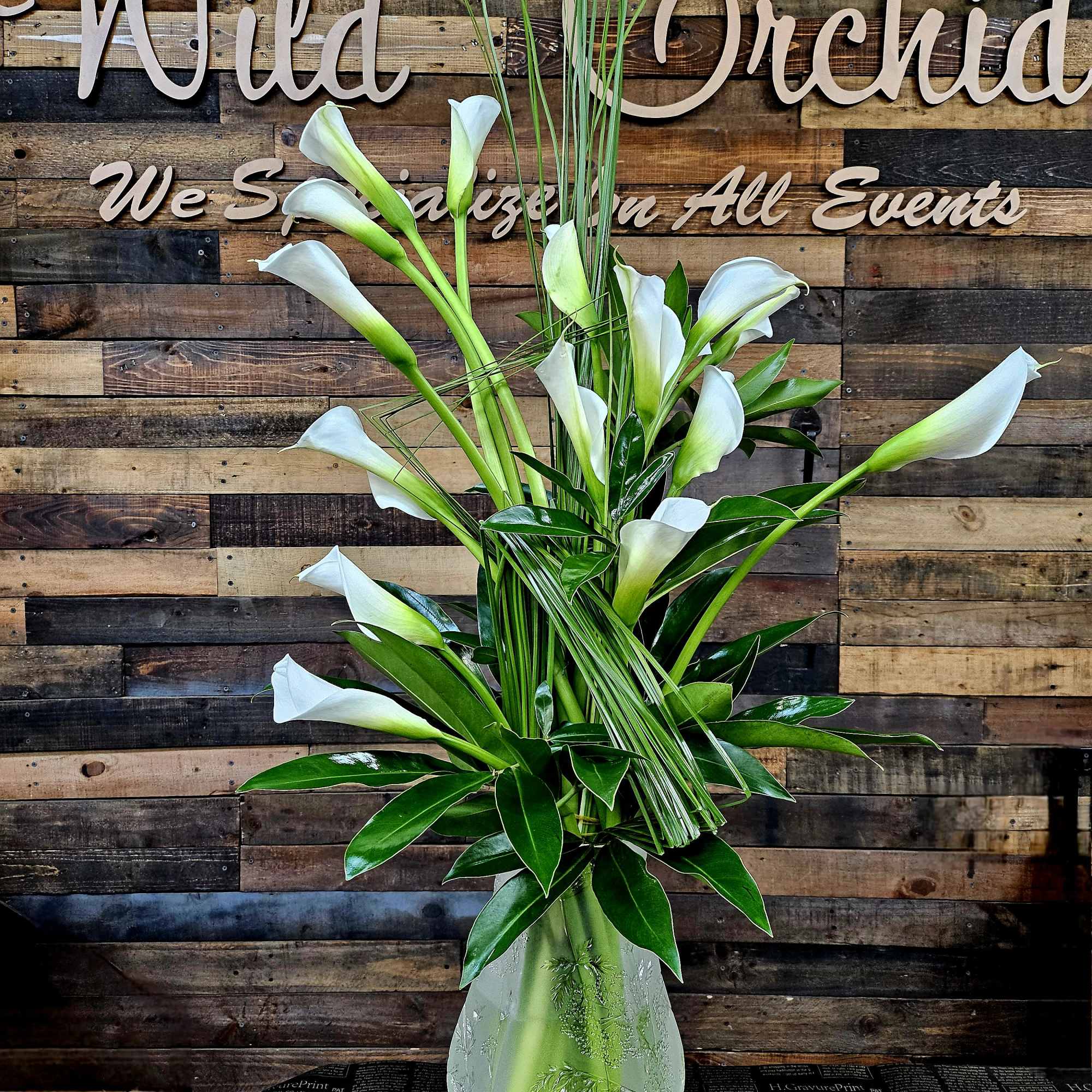 Tall arrangement of white calla lilies in a clear vase