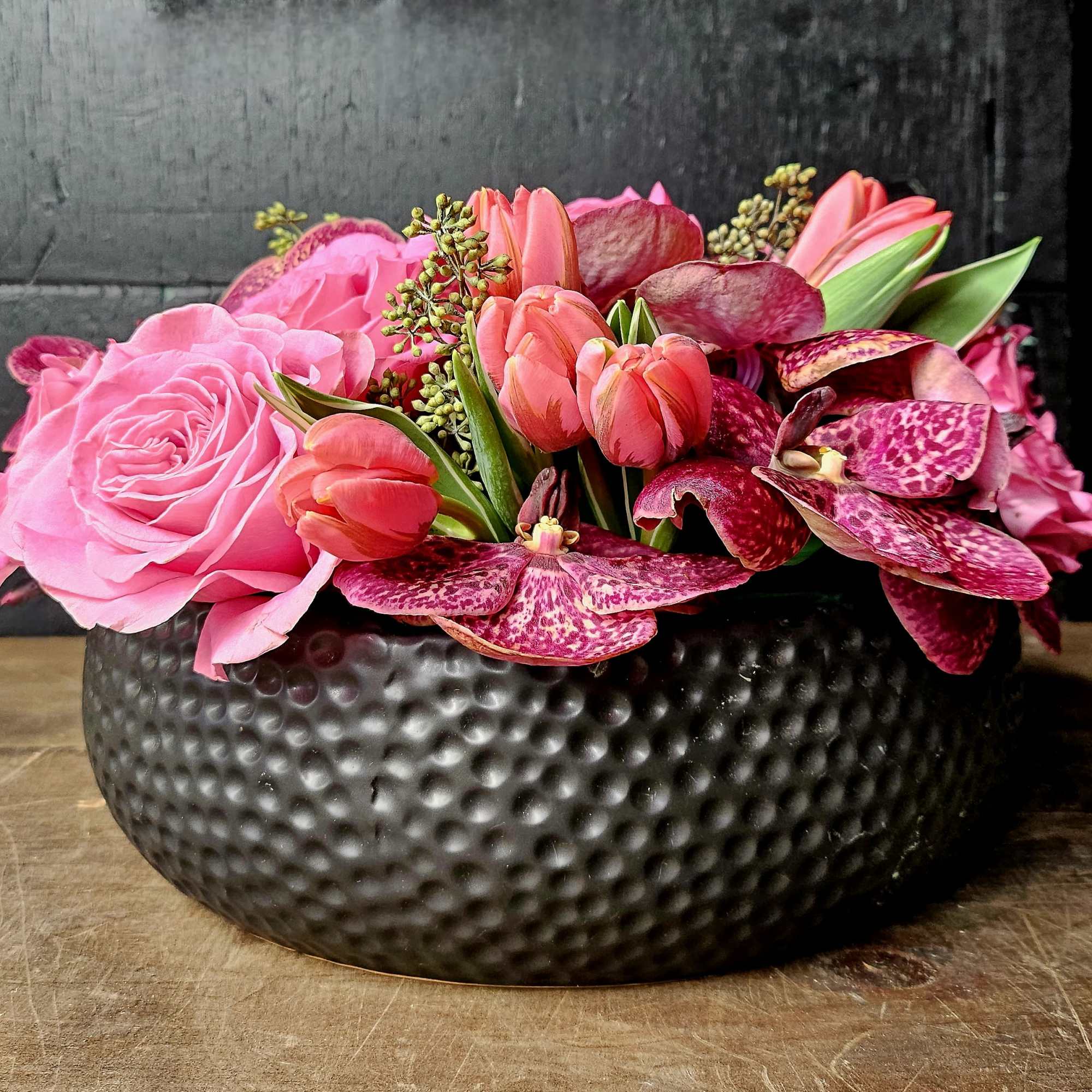 Pink roses and tulips arranged in a black textured bowl