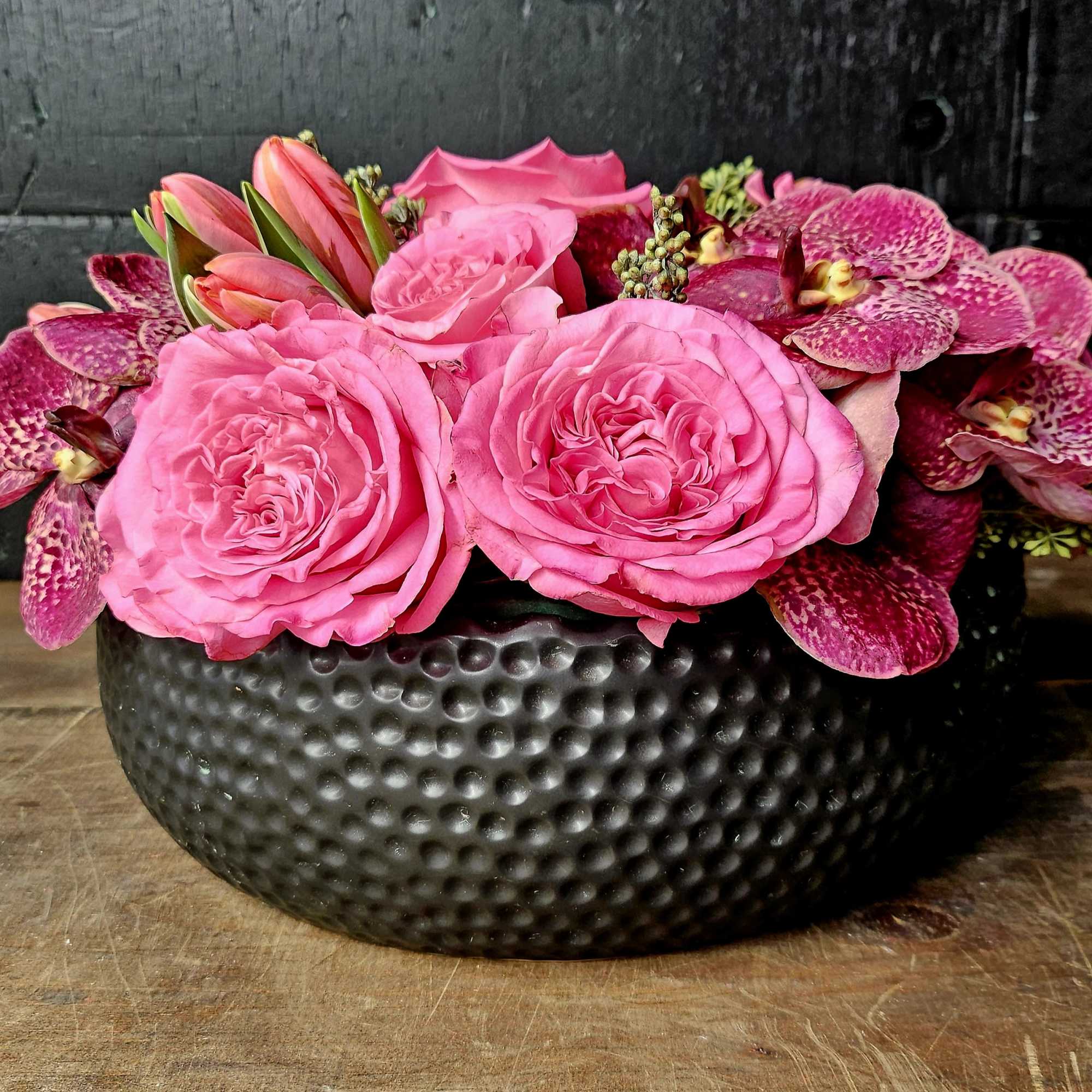 Pink roses and orchids arranged in a black bowl vase