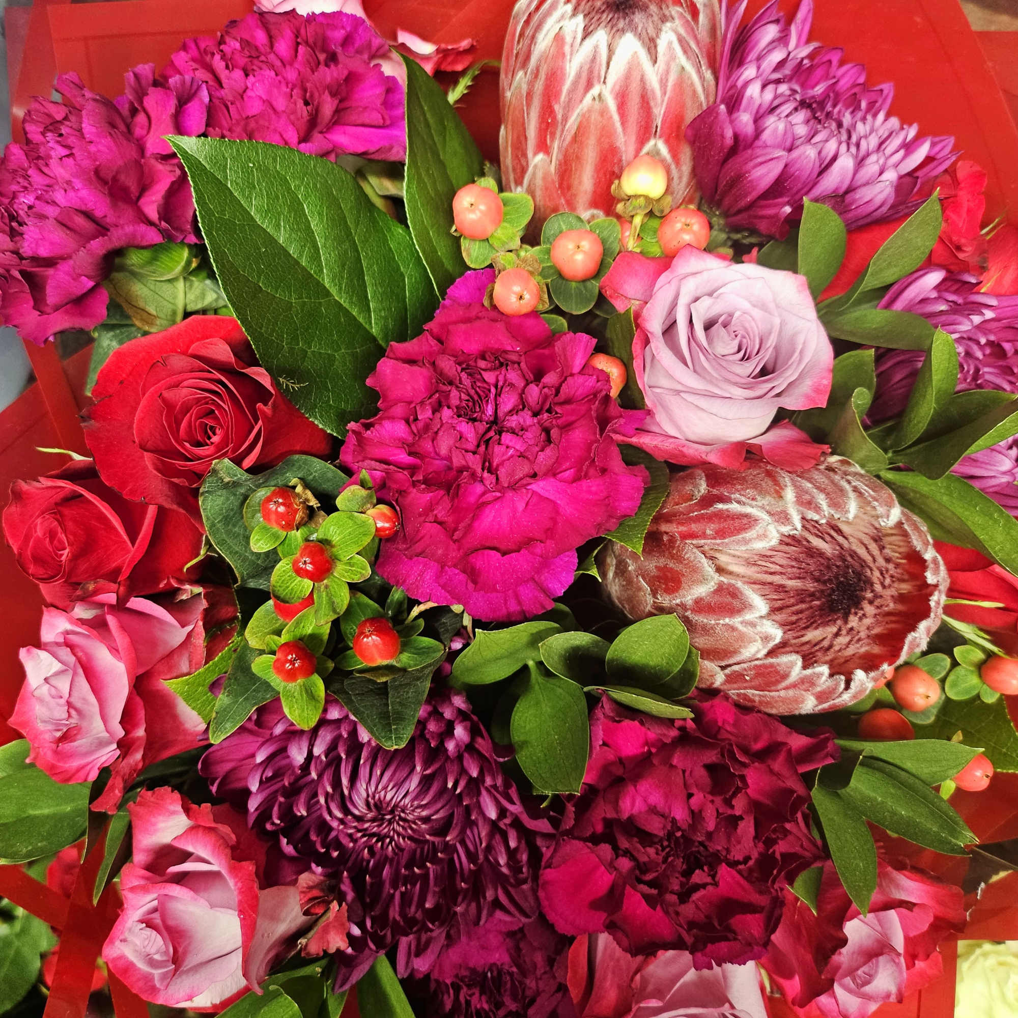 Bouquet of pink and purple flowers with red roses and green foliage