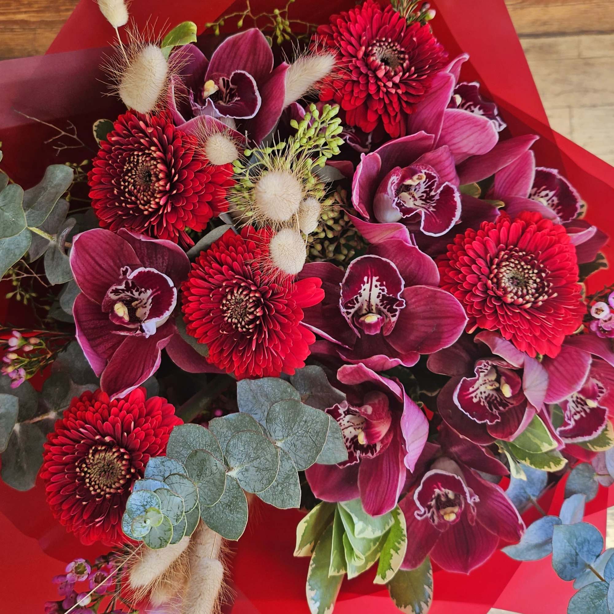 Bouquet of red gerbera daisies and magenta orchids wrapped in red paper
