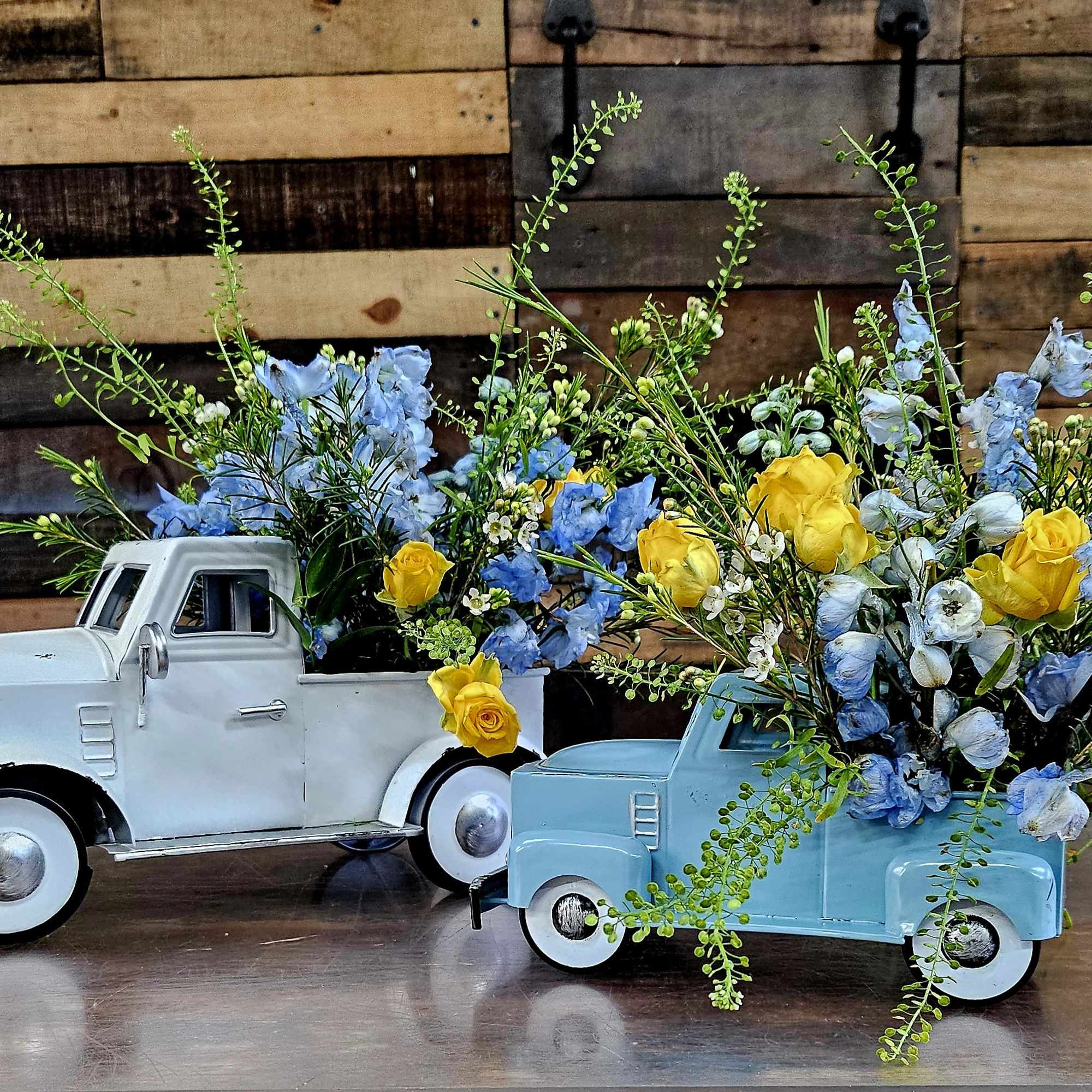 Two toy pickup trucks filled with blue and yellow flowers