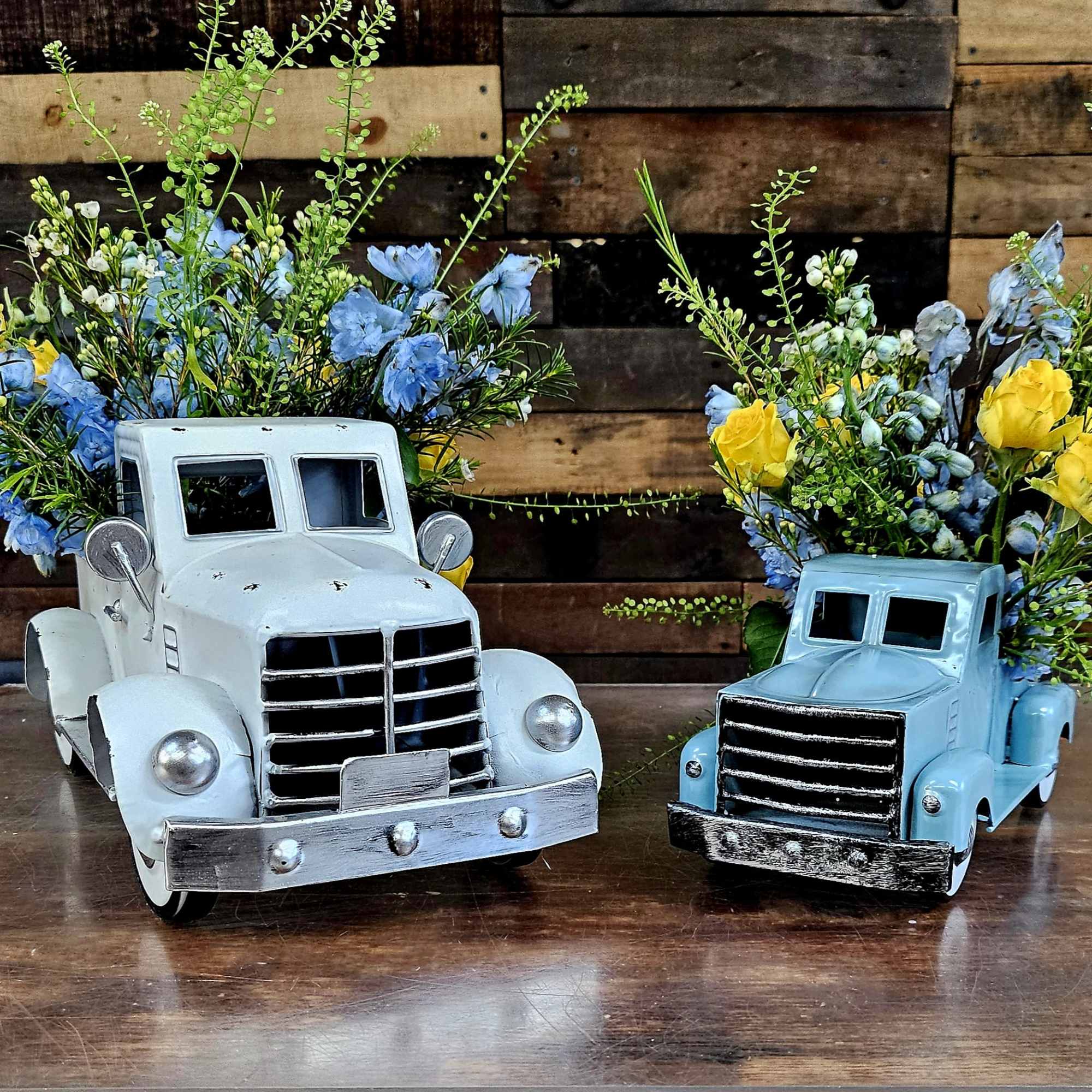 Two toy trucks filled with blue and yellow flowers on a wooden table