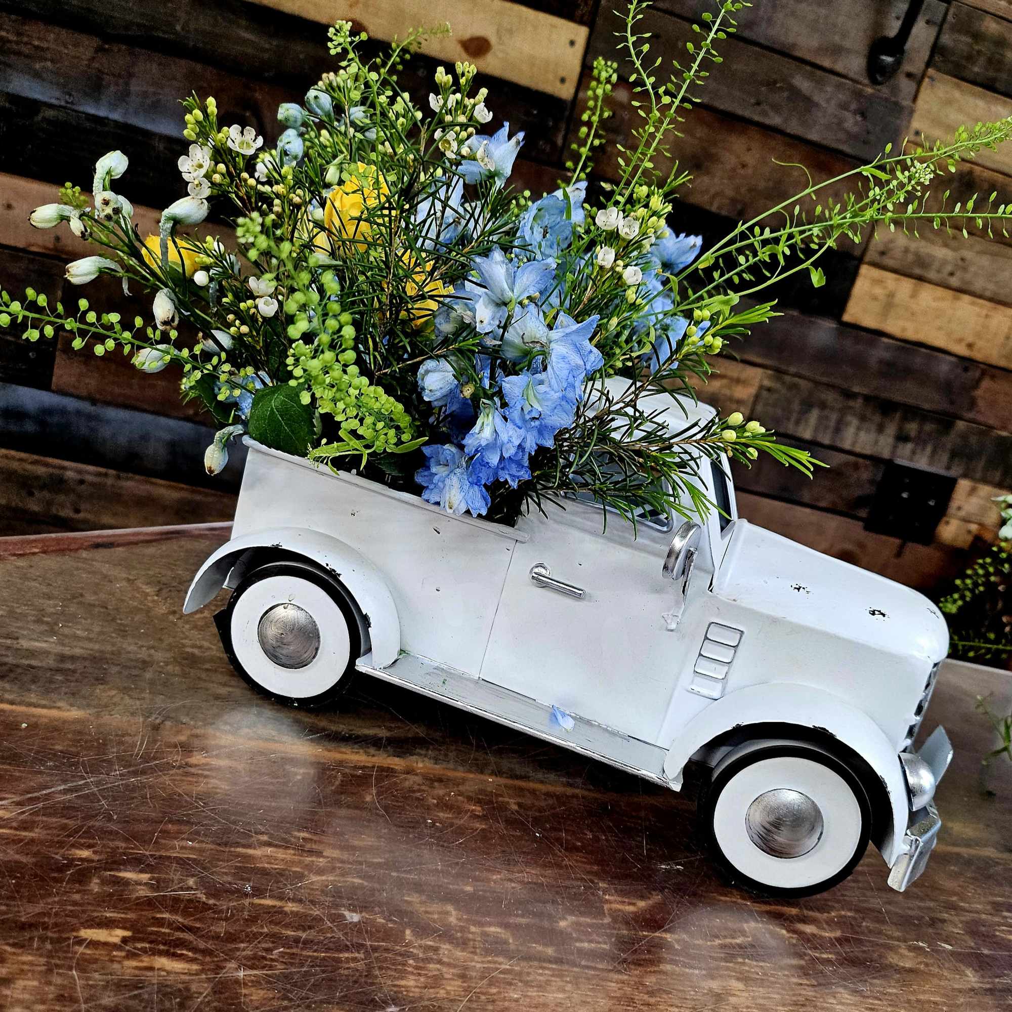 Blue and white flowers arranged in a white toy truck planter