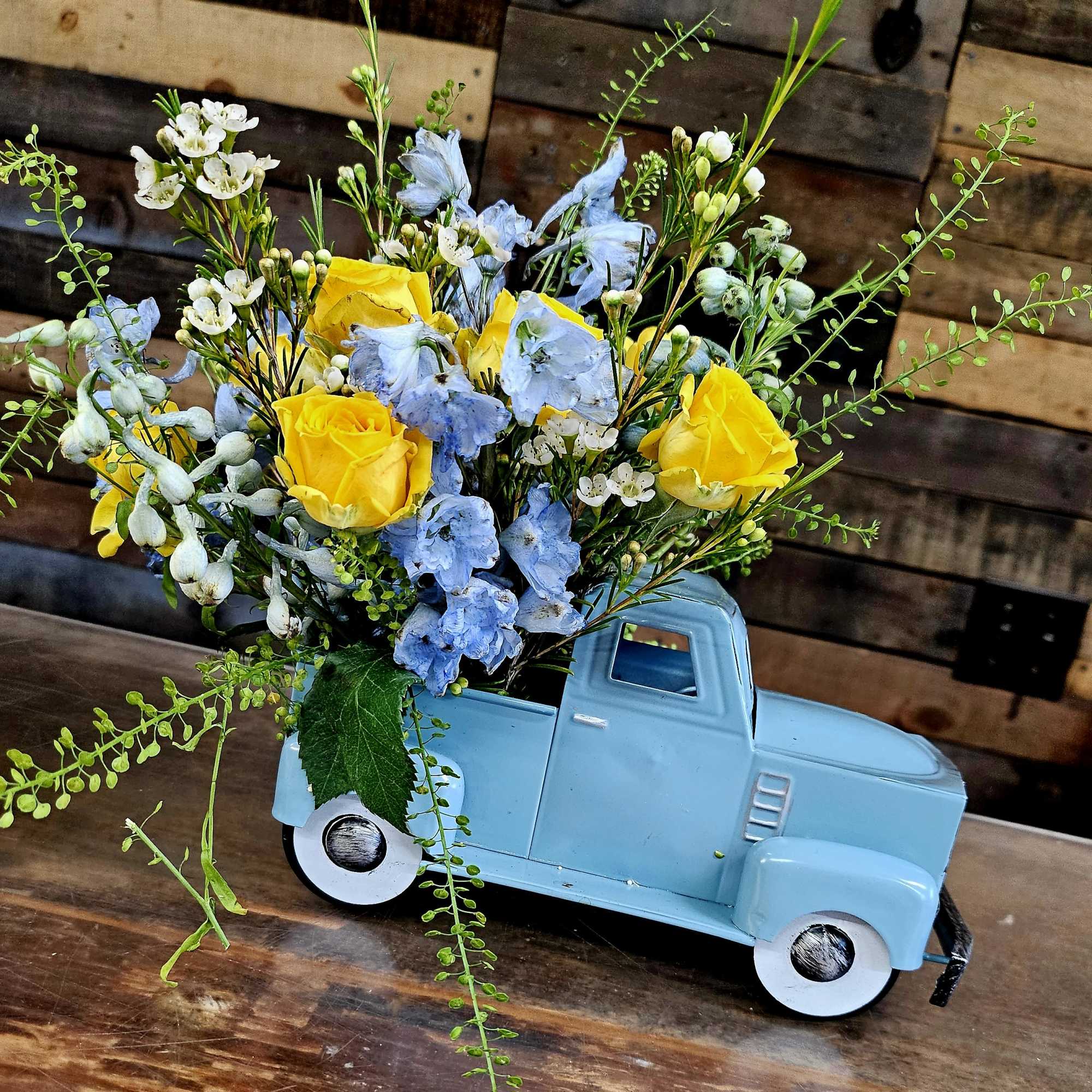 Yellow and blue flowers arranged in a light blue truck-shaped container