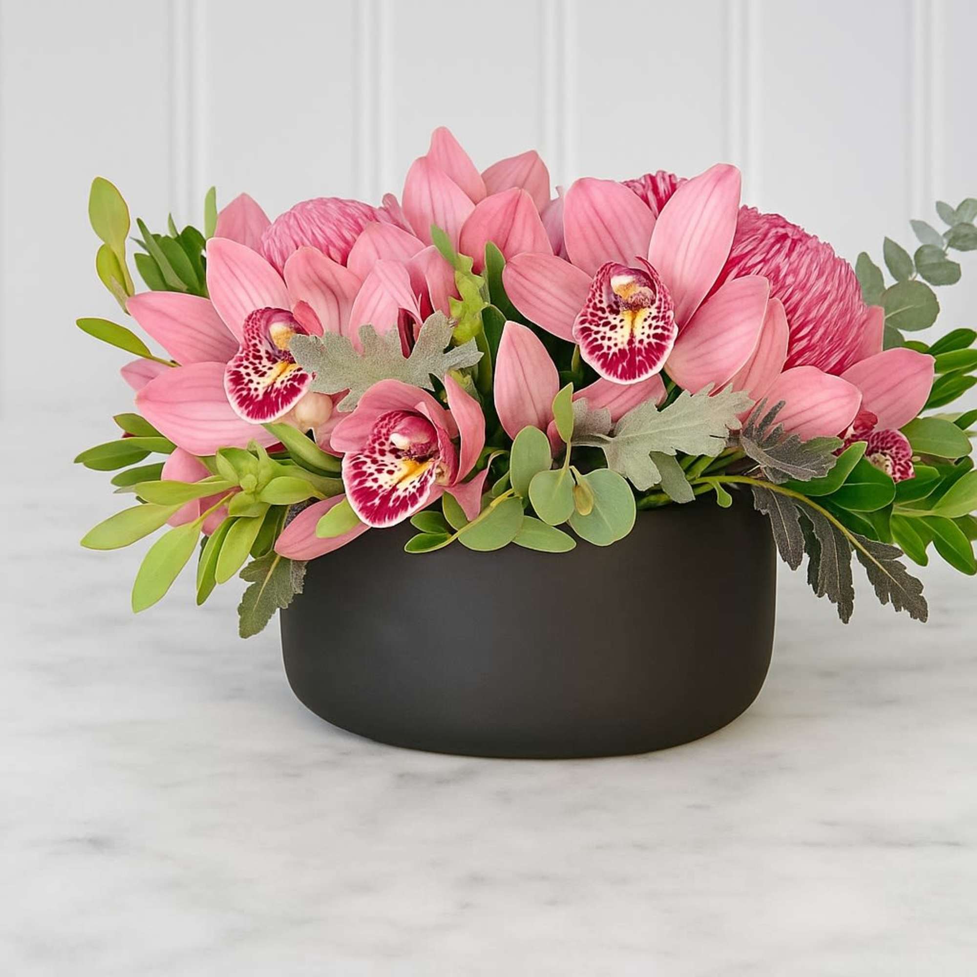 Pink orchid and chrysanthemum arrangement in a black bowl
