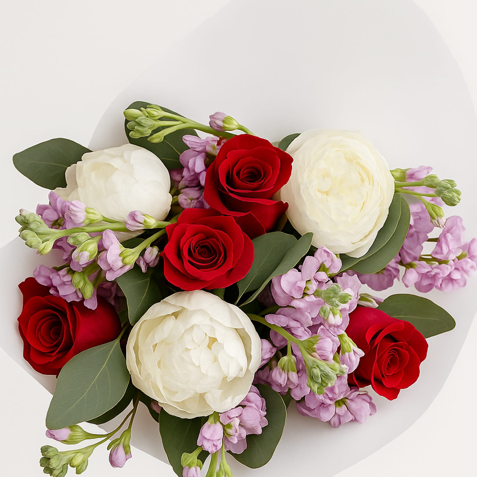 Bouquet of red roses, white ranunculus, and lavender flowers in white paper